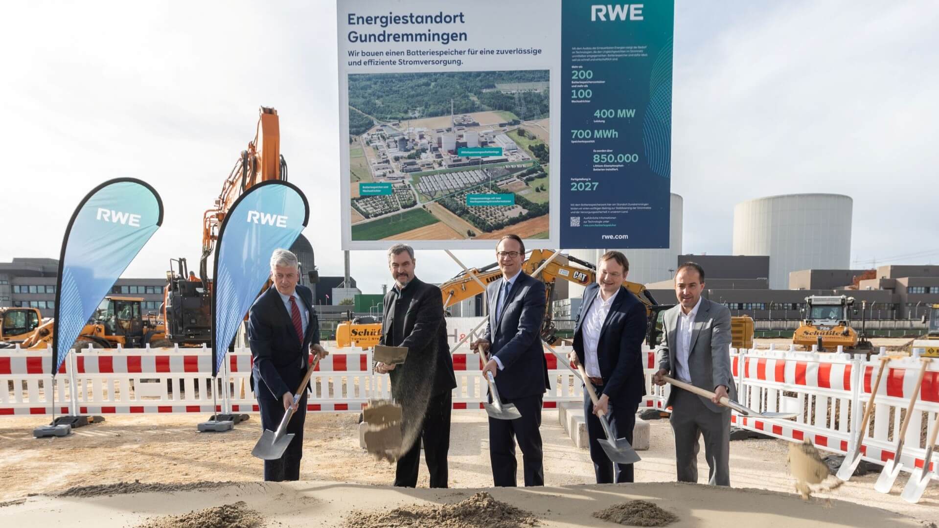Five men with shovels standing in front of a sign