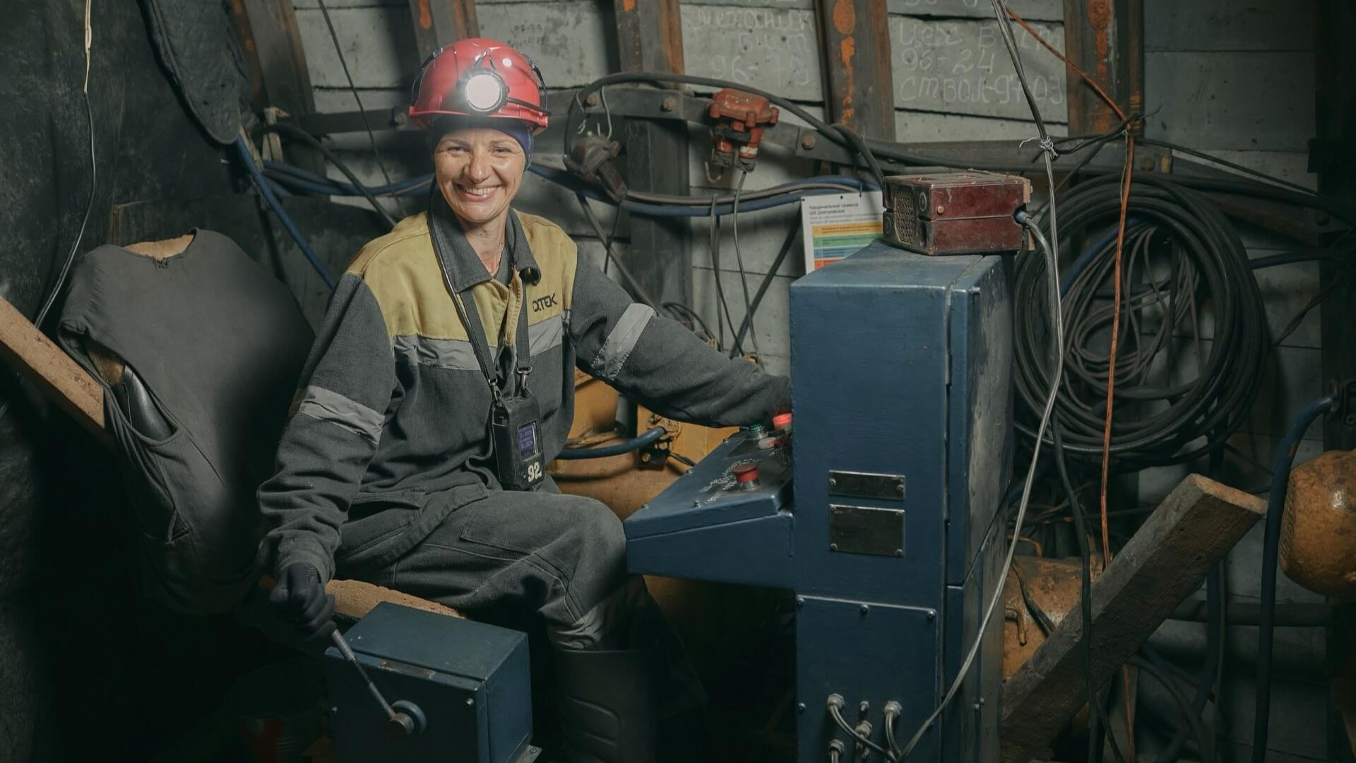 Smiling woman miner in hard hat sitting and operating equipment in underground mine