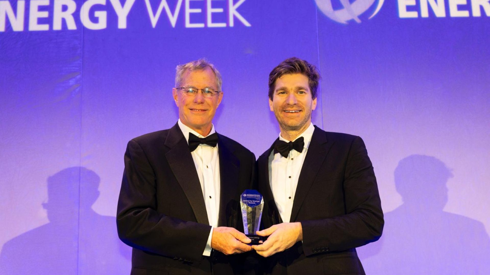Two men in dinner jackets, standing side by side, holding a glass award and smiling to camera