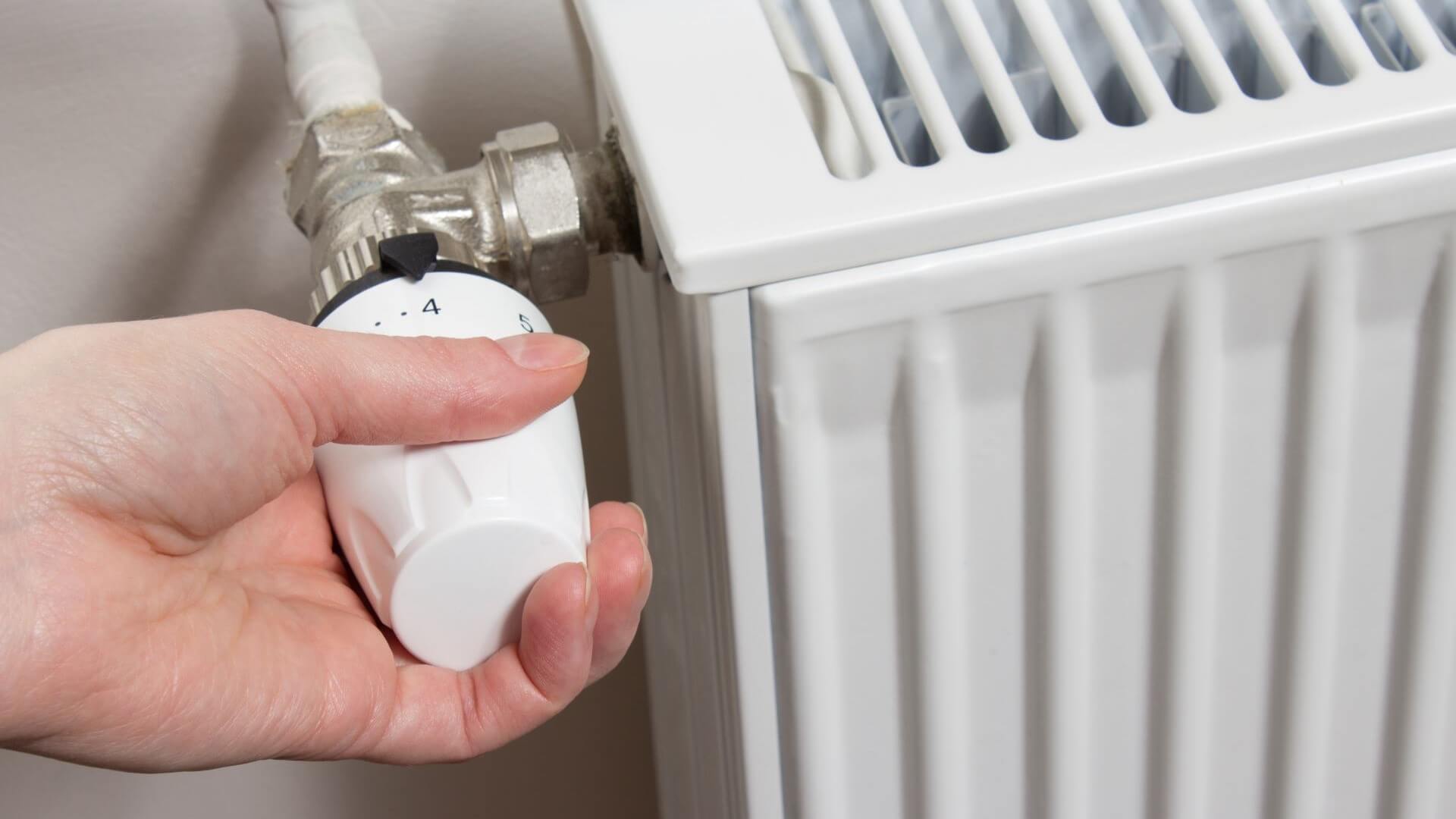 Close up of hand turning down temperature thermostat valve on radiator