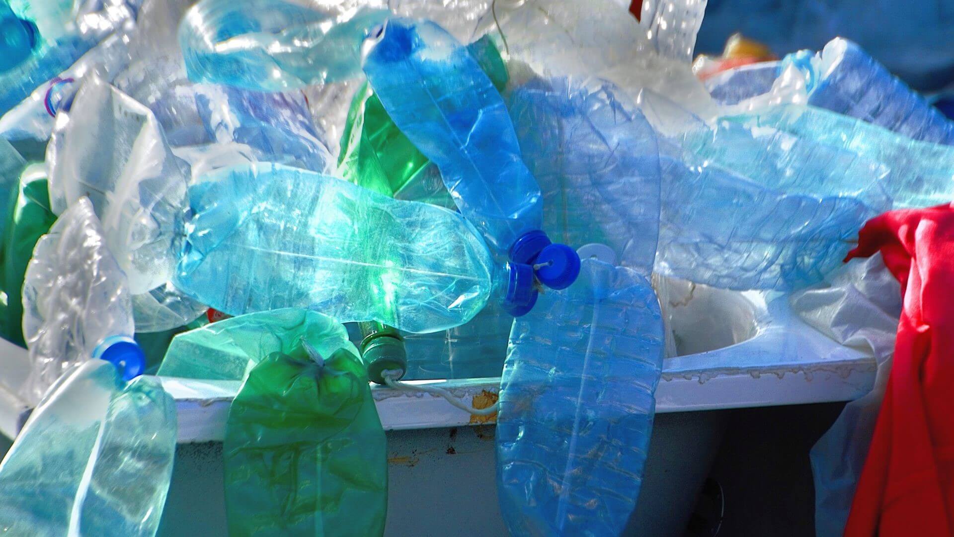 Close up of blue, green and clear plastic drinks bottles spilling over the side of a large waste bin