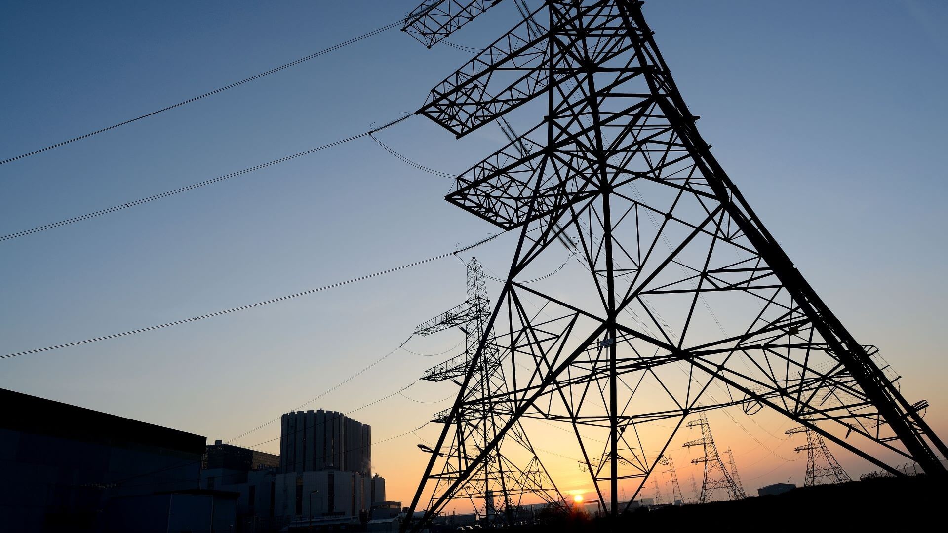 Silhouette of Dungeness nuclear power station against sunset with electricity pylon in foreground