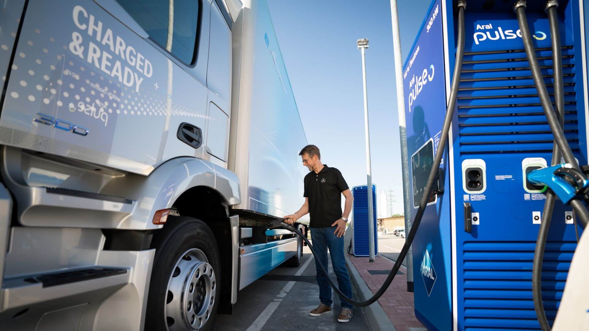 Man standing by large truck, plugging in electric charger