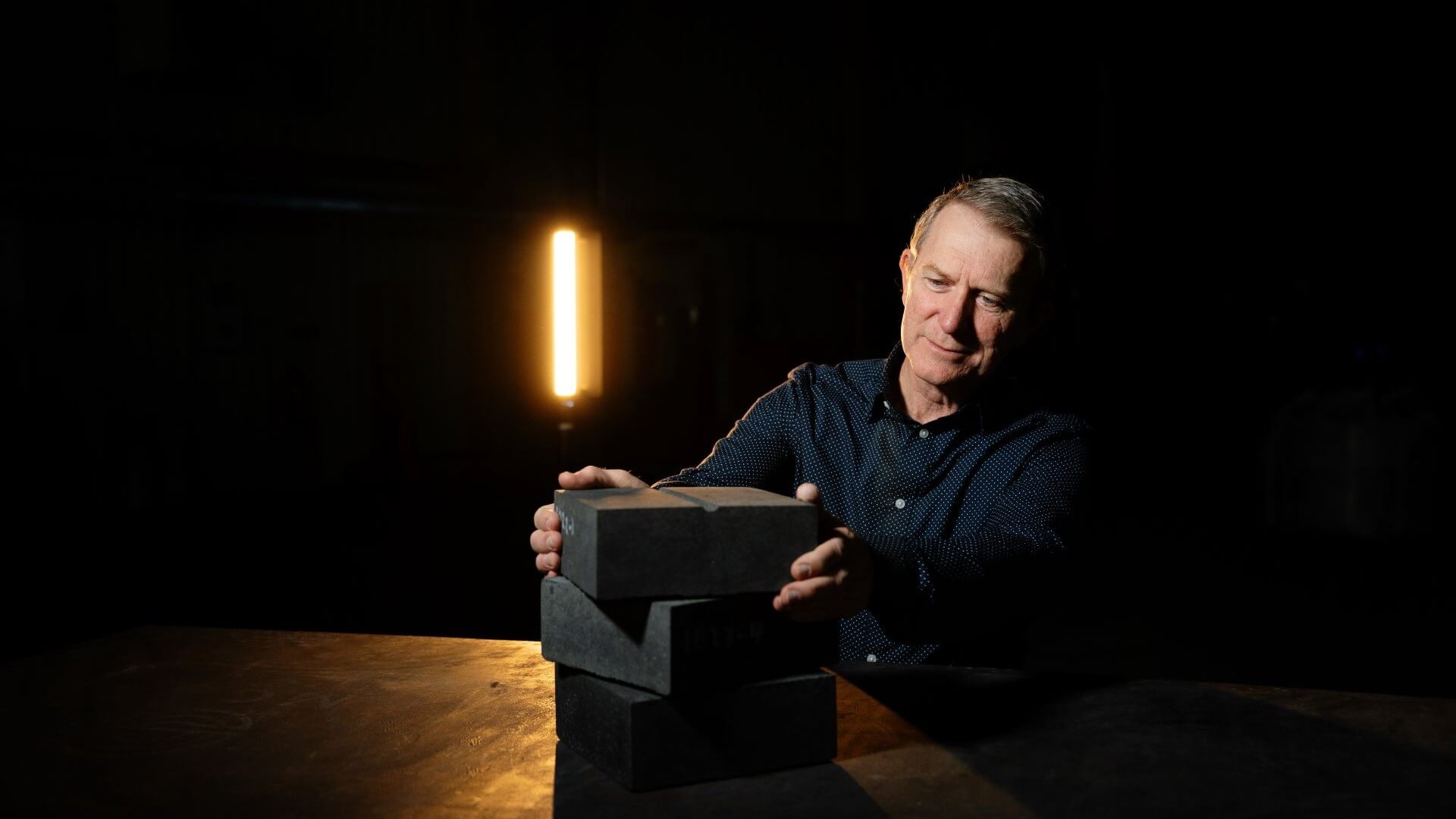 MGA Thermal CEO Erich Kisi set against black backdrop, holding grey coloured thermal energy storage blocks made with miscibility gap alloys
