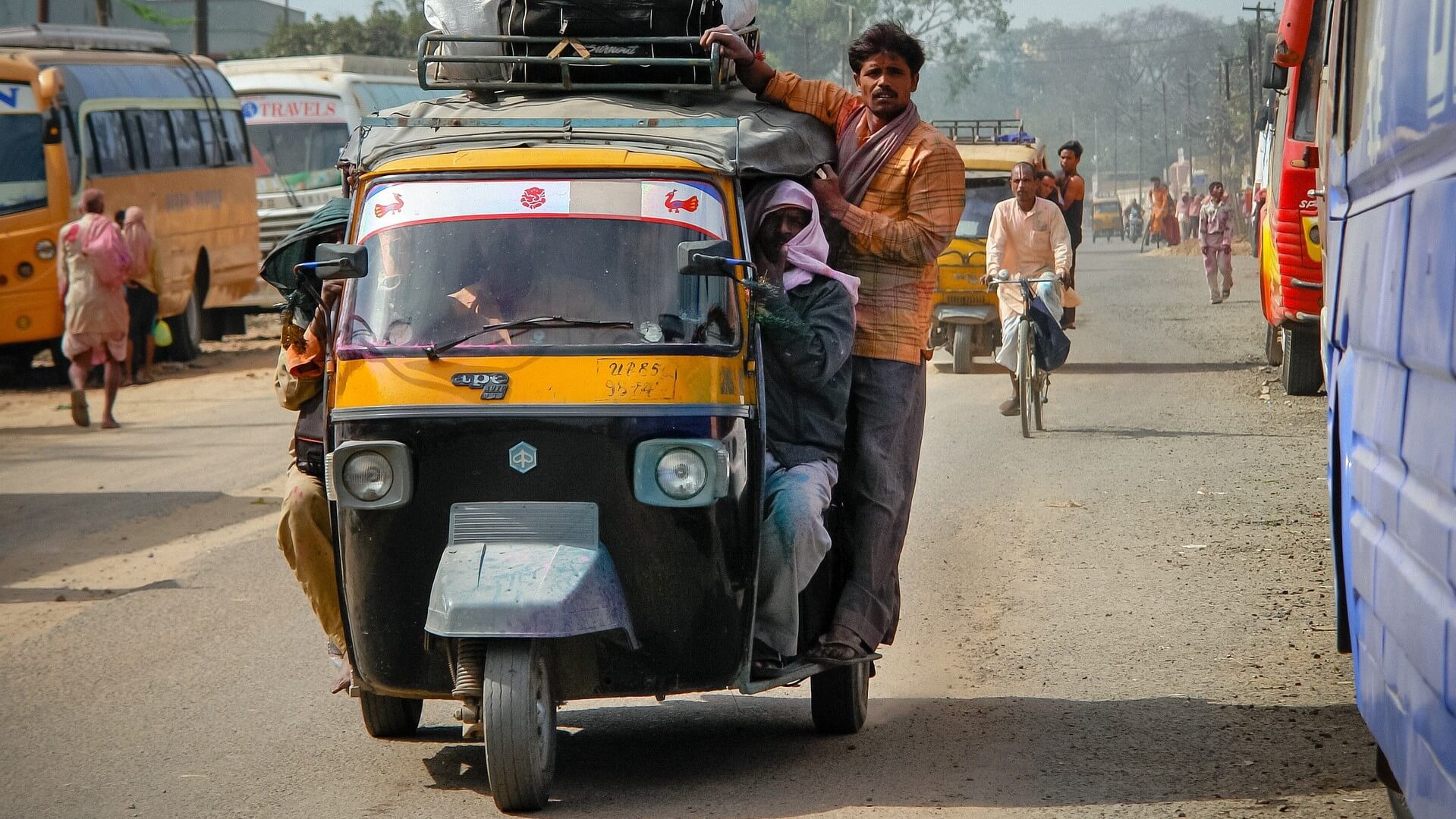 Three-wheel tuk tuk on Indian road, with passenger hanging on to the side