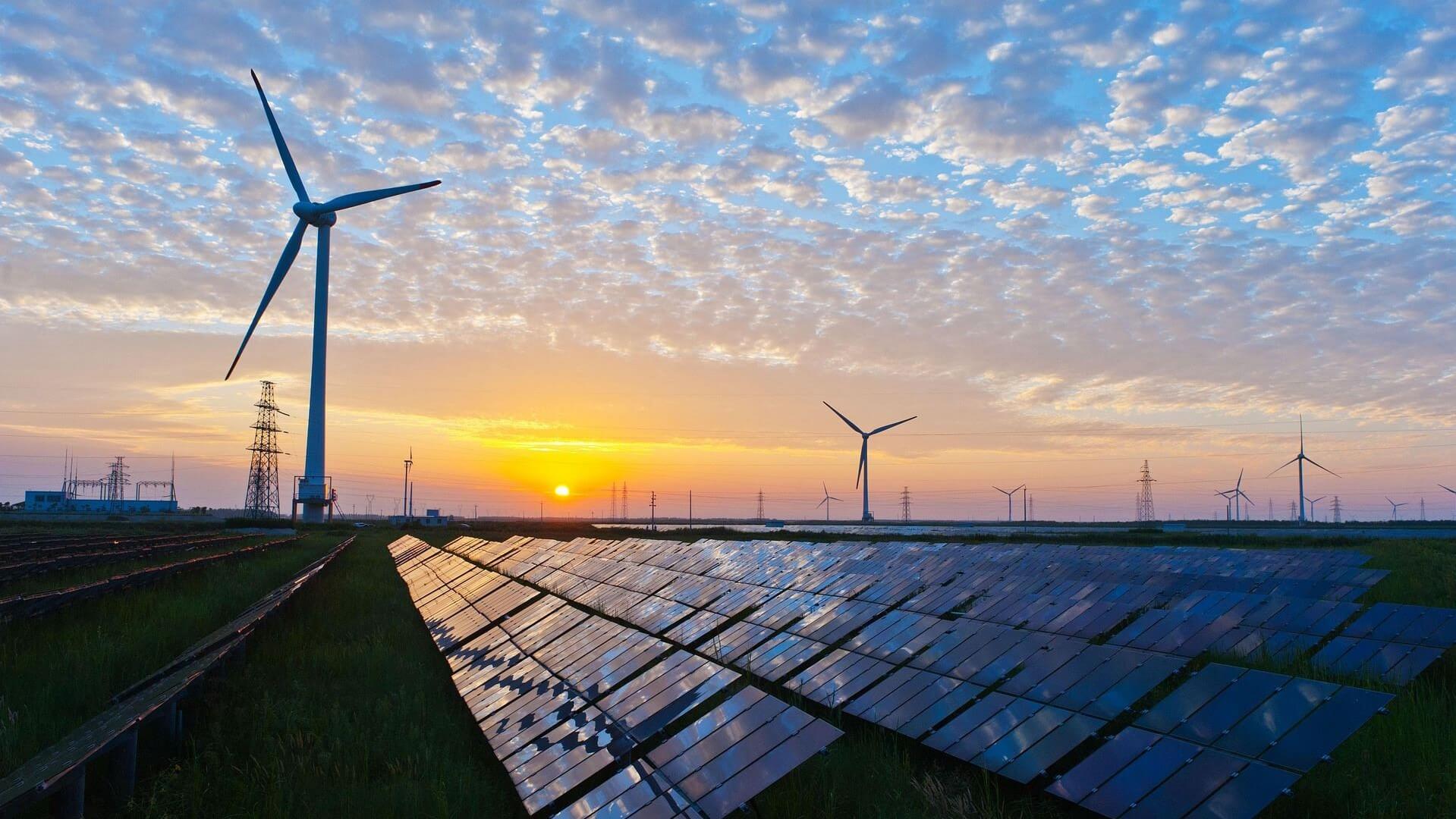 Solar panels in foreground, wind turbines in mid and background, set against sunrise sky