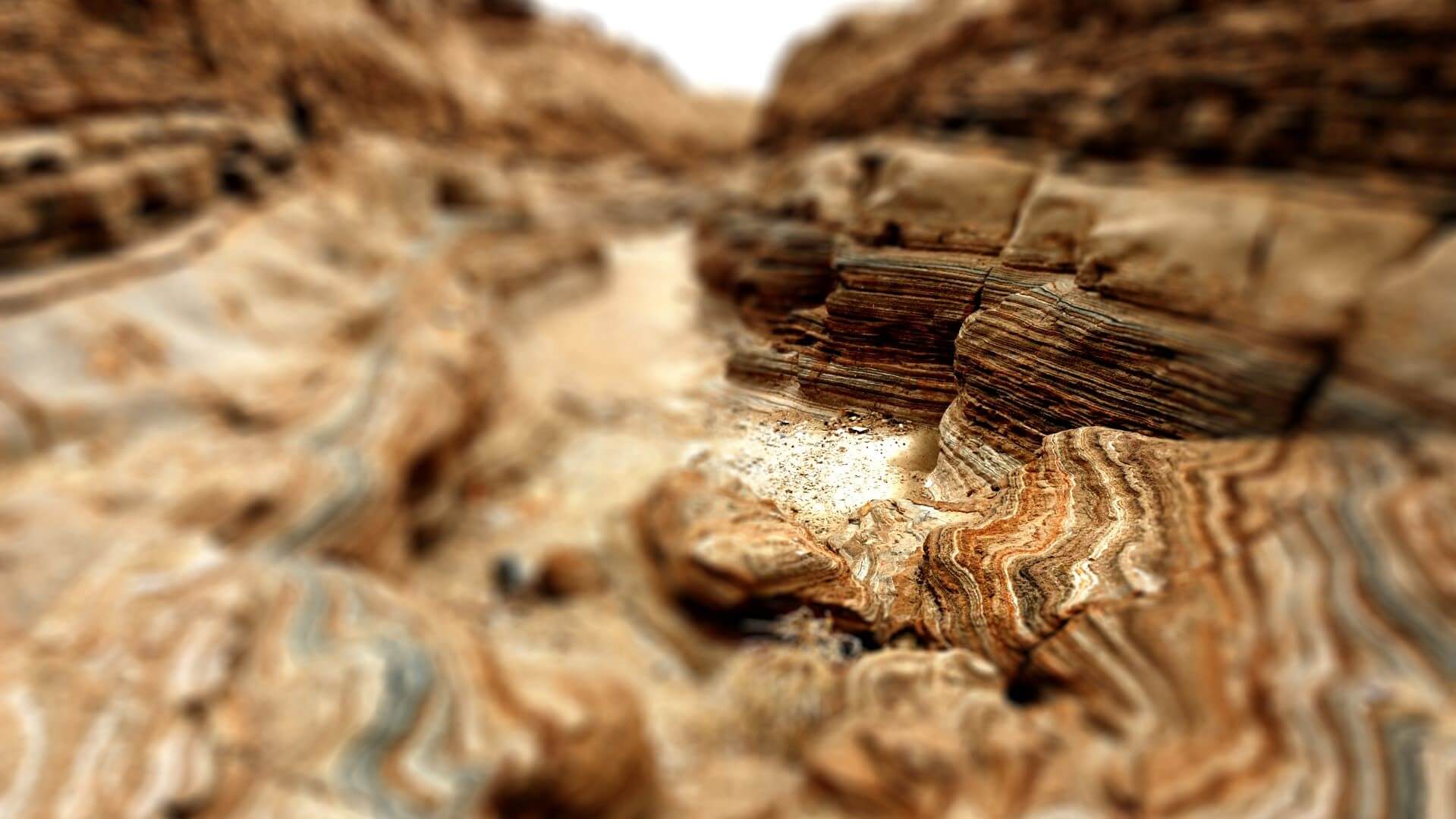 Aerial view over alternating layers of sands and shale exposed through erosion, with blurred focus on edges of pic