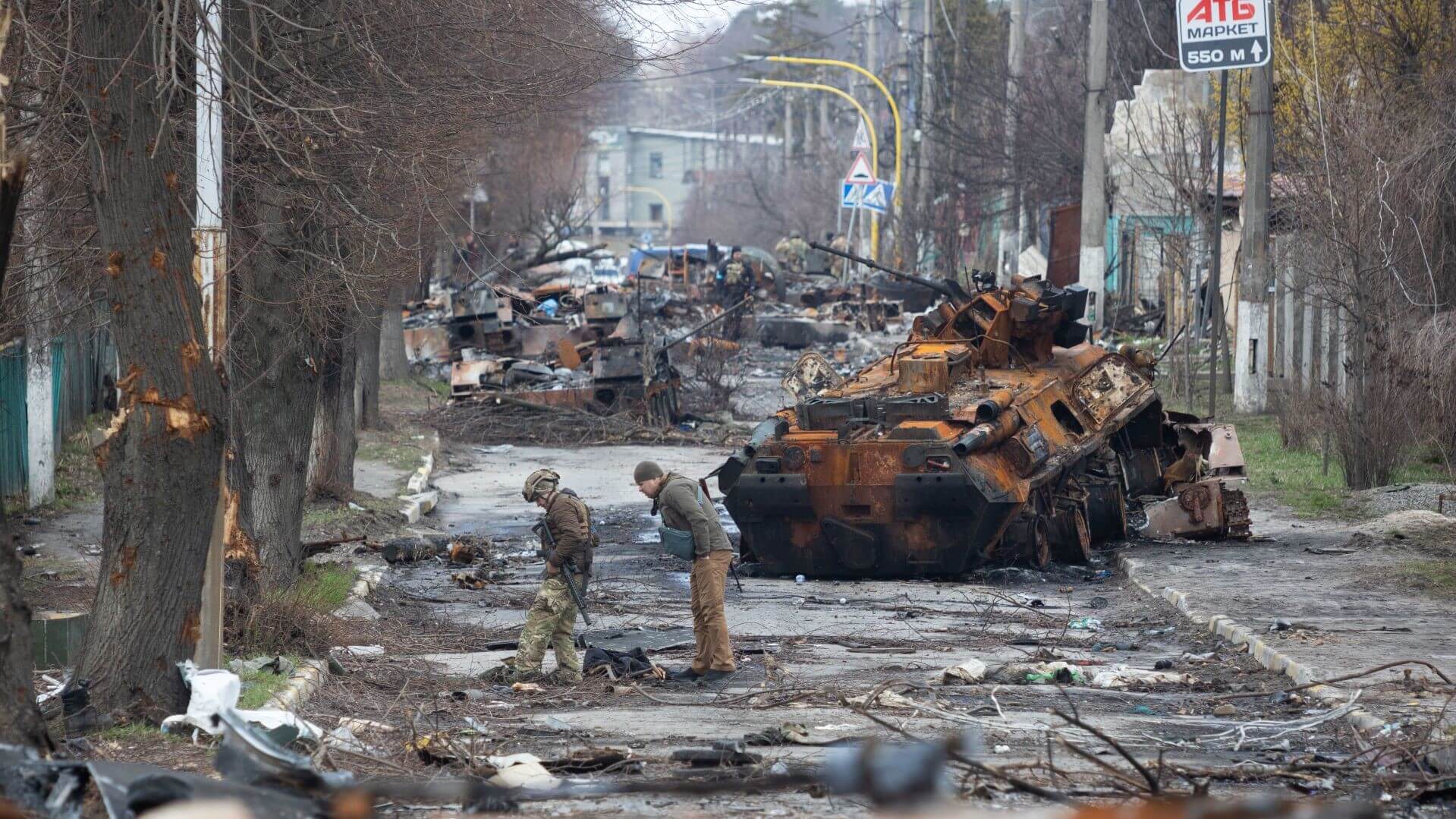 Two soldiers in war torn street, burnt out tanks and vehicles in background