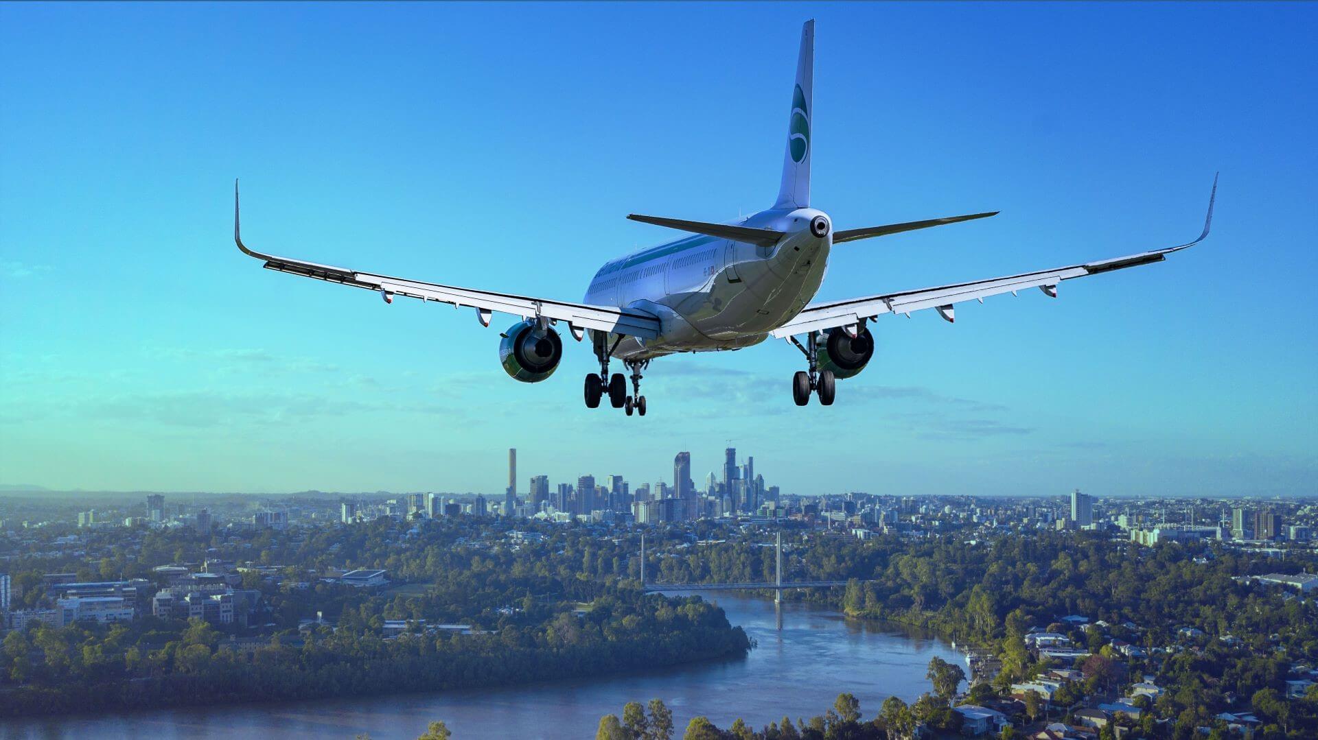 Aeroplane flying above river running through city, against blue sky