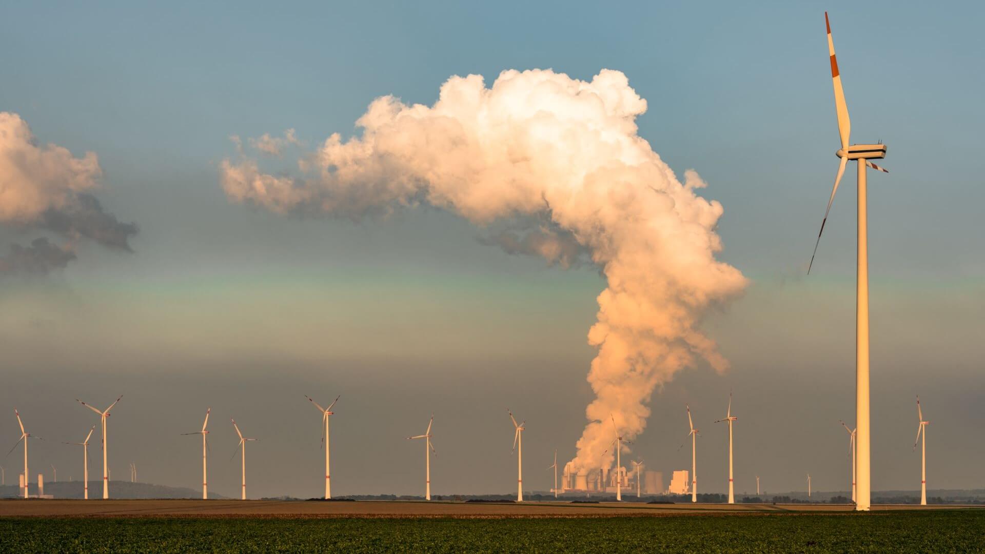 Group of wind turbines in front of coal-fired power station emitting clouds of smoke