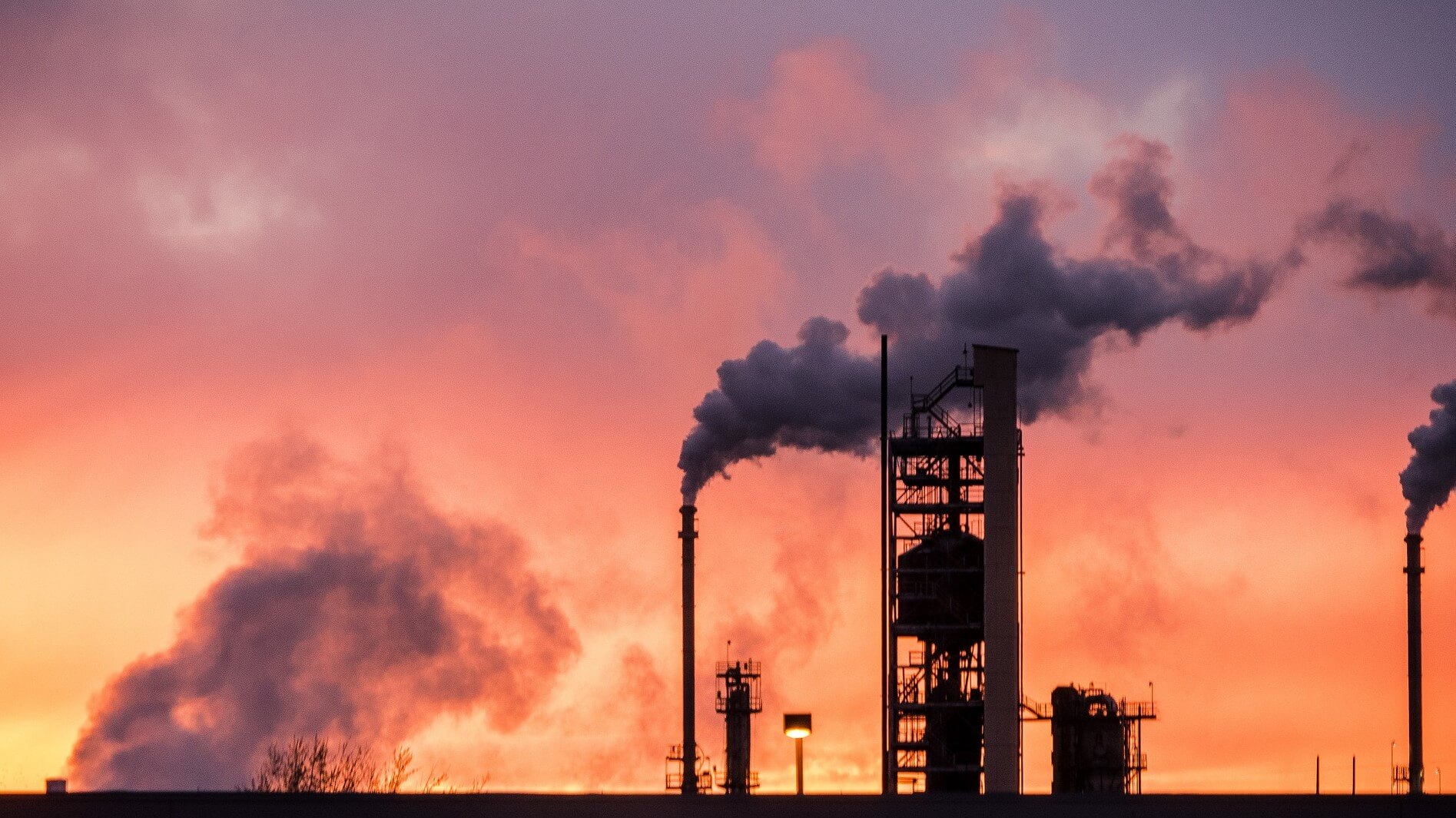 Oil and gas facilities silhouetted against orange sunset sky