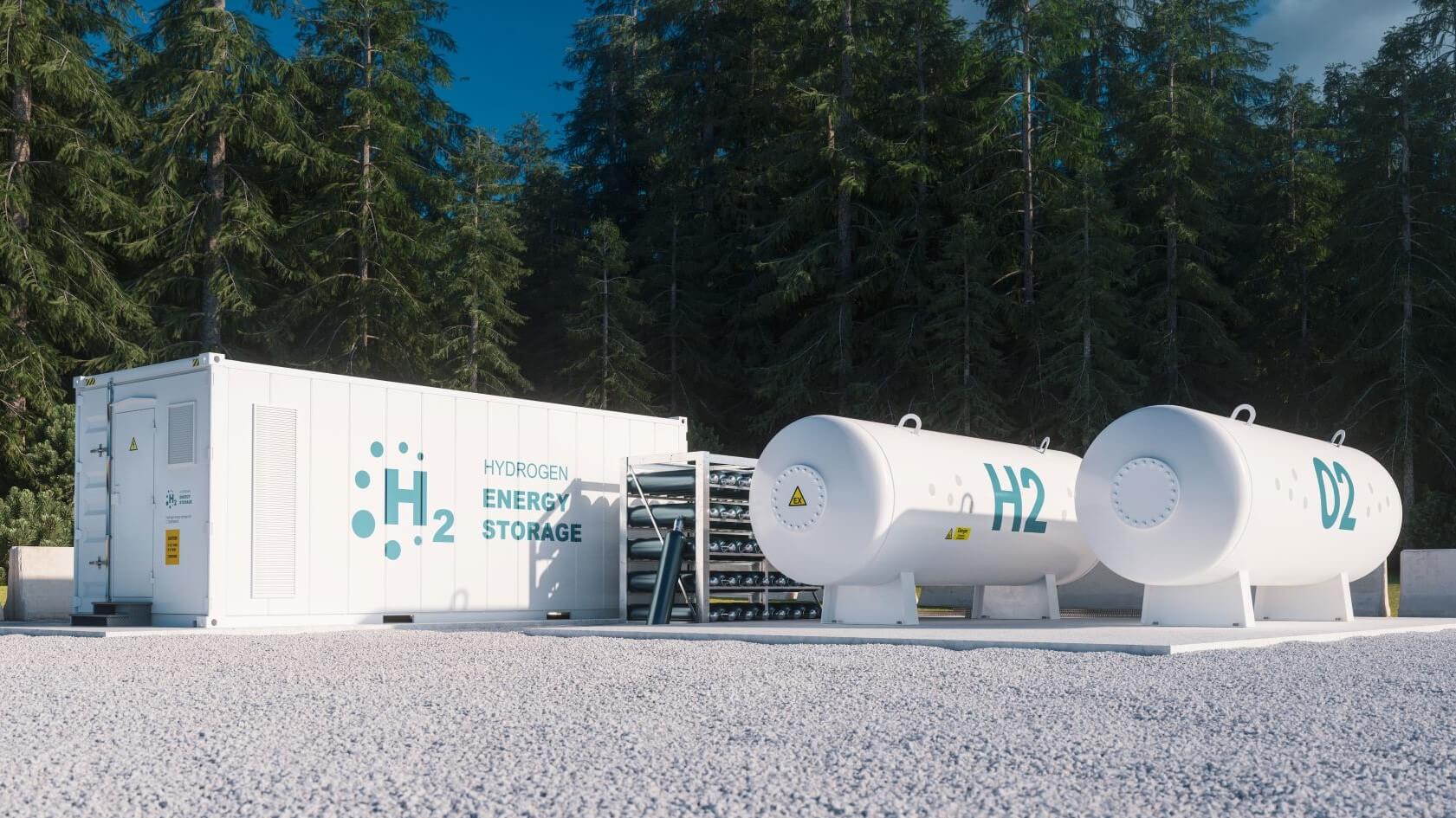 A range of rectangular and cylindrical hydrogen storage tanks on gravel surface with trees behind
