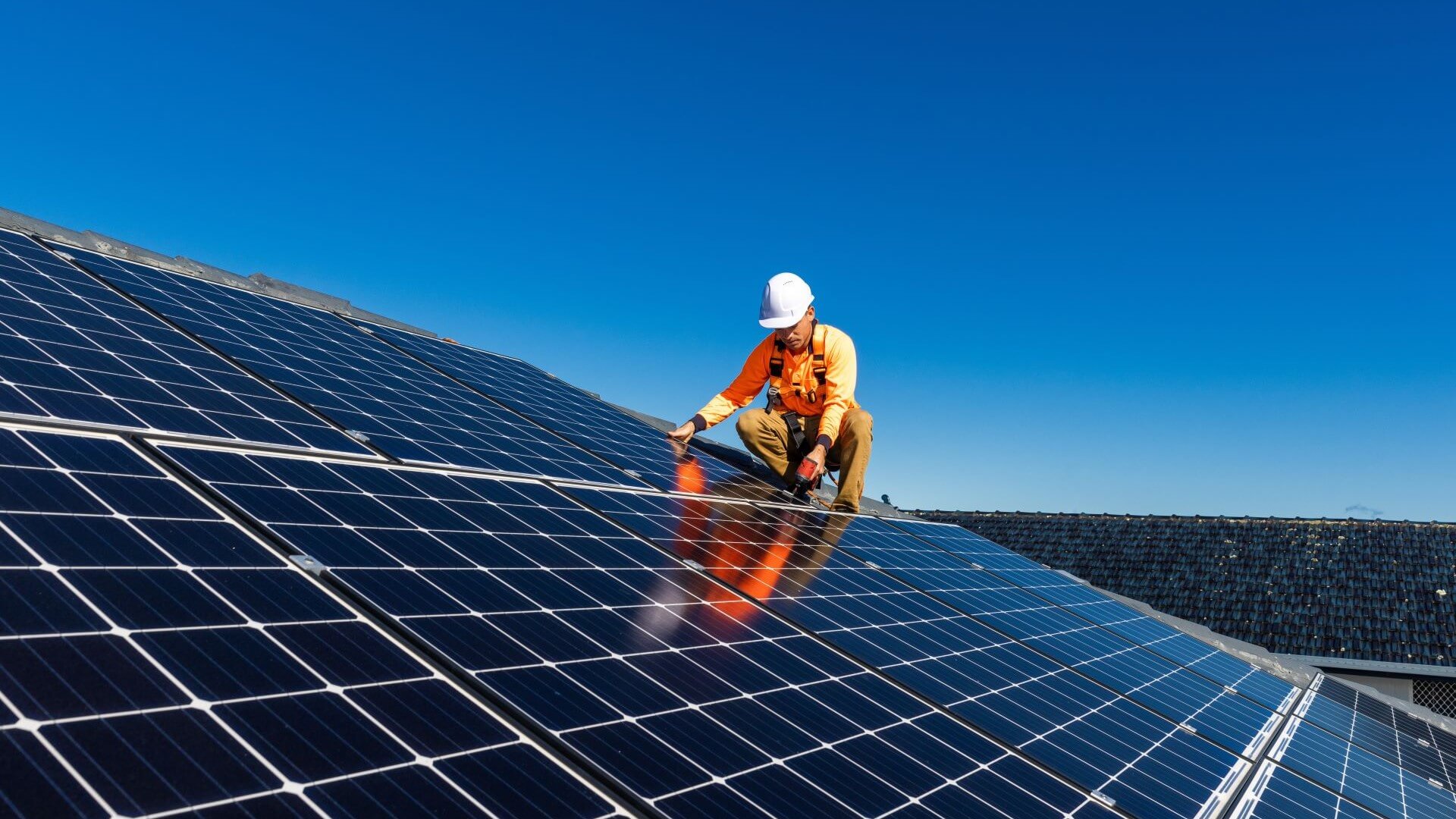 Man on roof covered with solar panels, set against bright blue sky