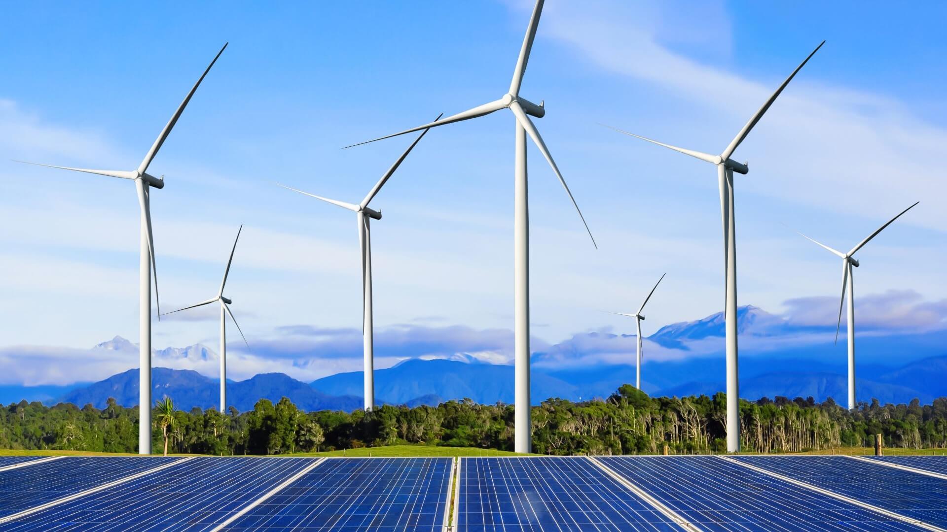 Wind turbines and solar panels in foreground against mountainous landscape