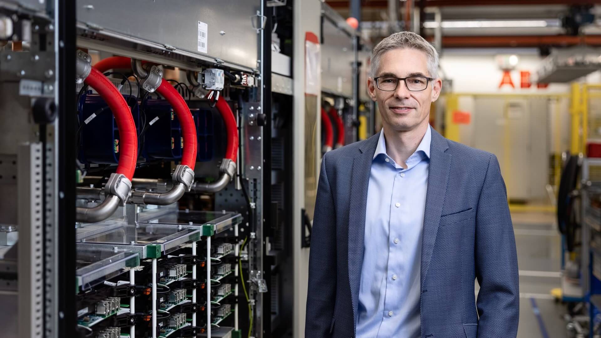 Photo of Adrian Guggisberg, Division President, ABB Motion Services, from waist up, standing in front of industrial equipment