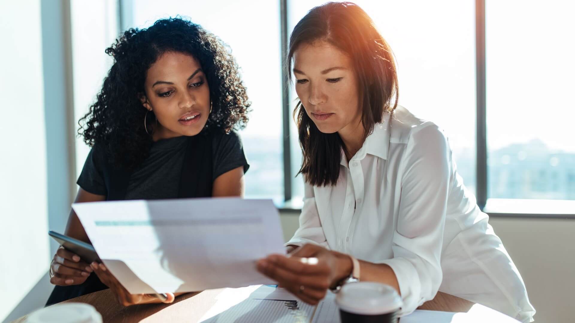 Two women discussing document together in sun lit office