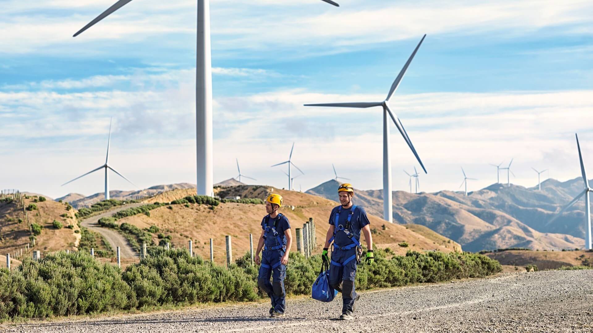 Two engineers walking beside wind turbines in mountainous region, New Zealand