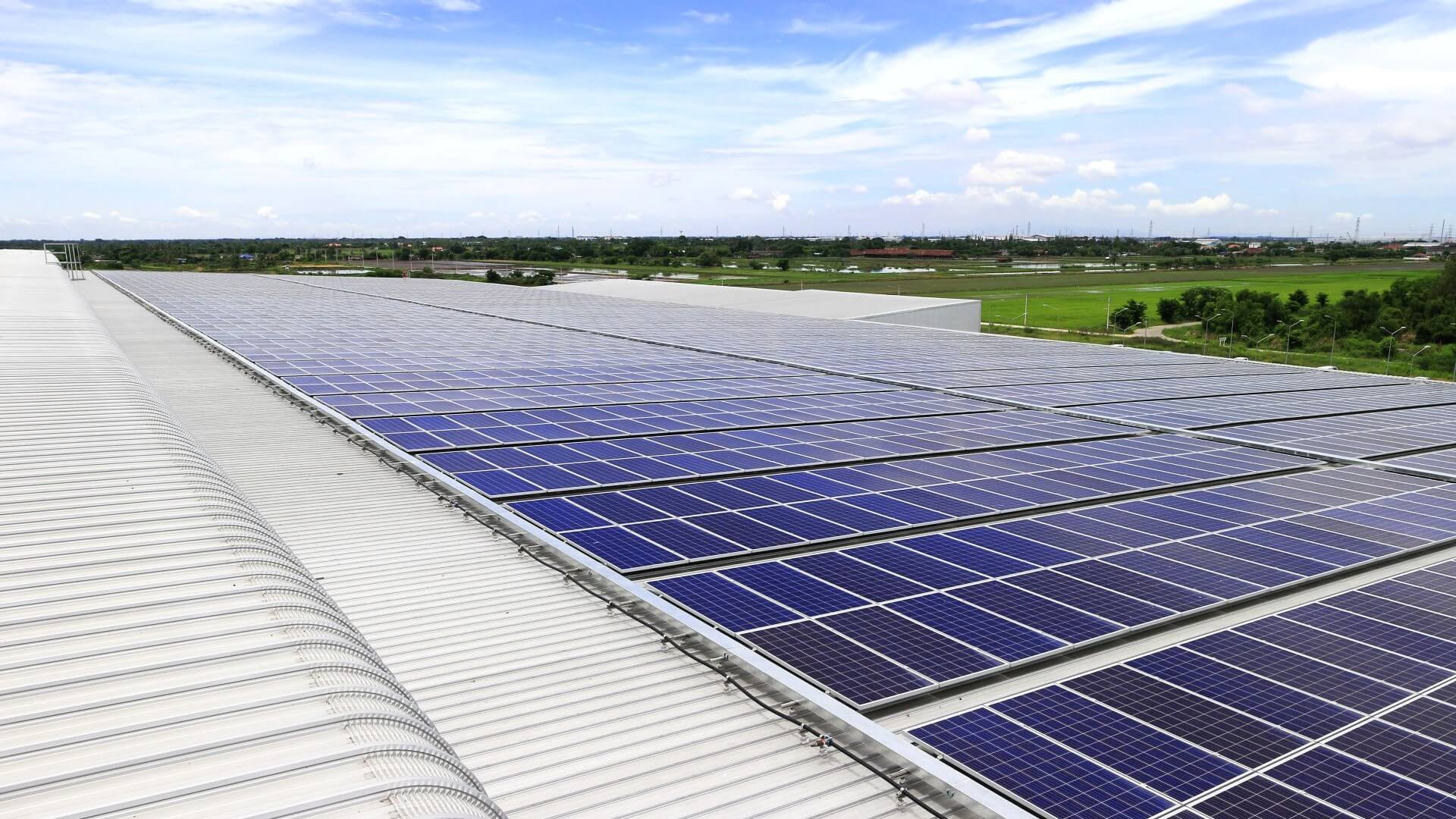 Close up of solar panels on rooftop, with green fields and blue sky in background