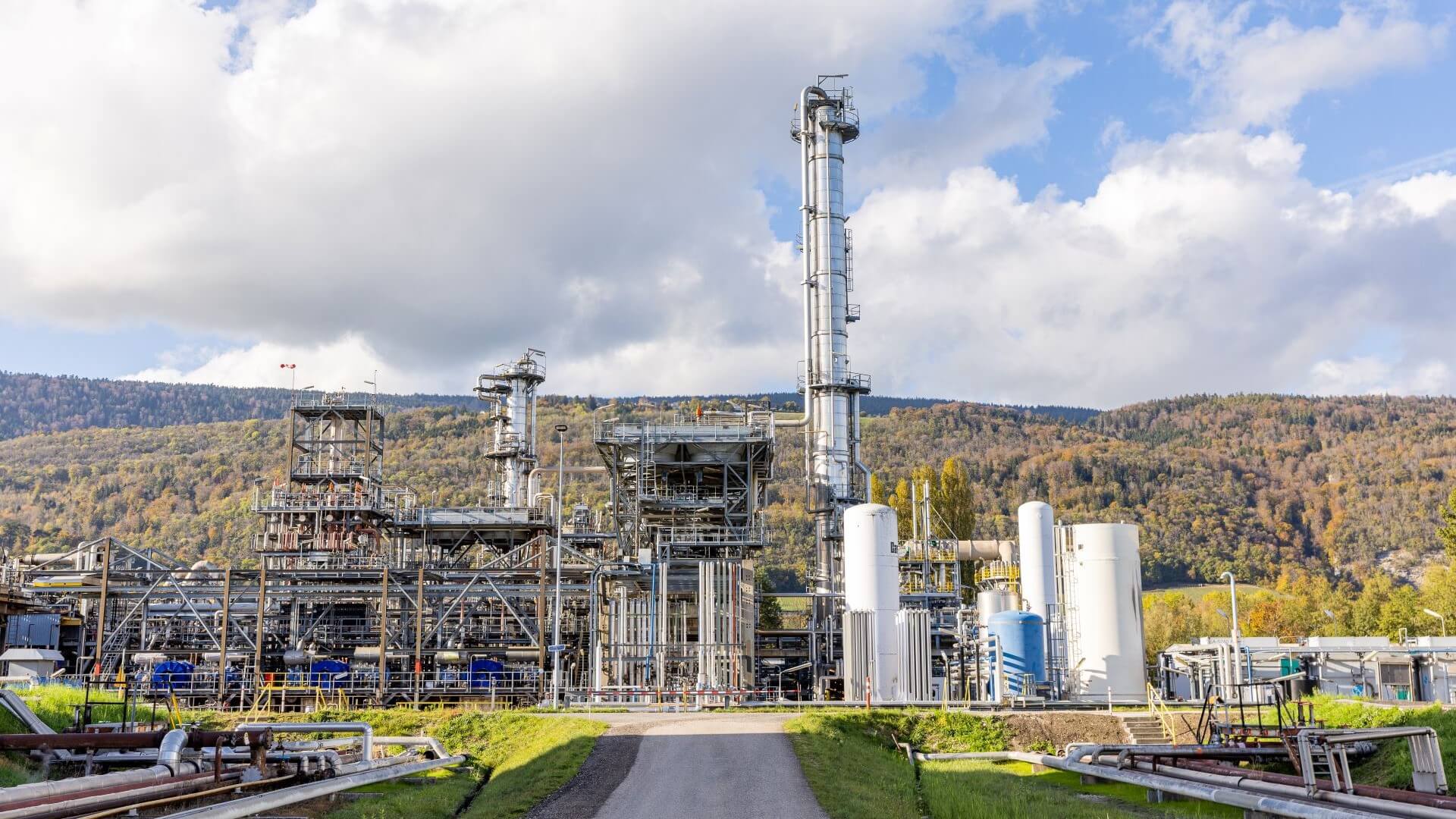 View of biogas facility, buidings and pipework, in green countryside and blue sky and white clouds above