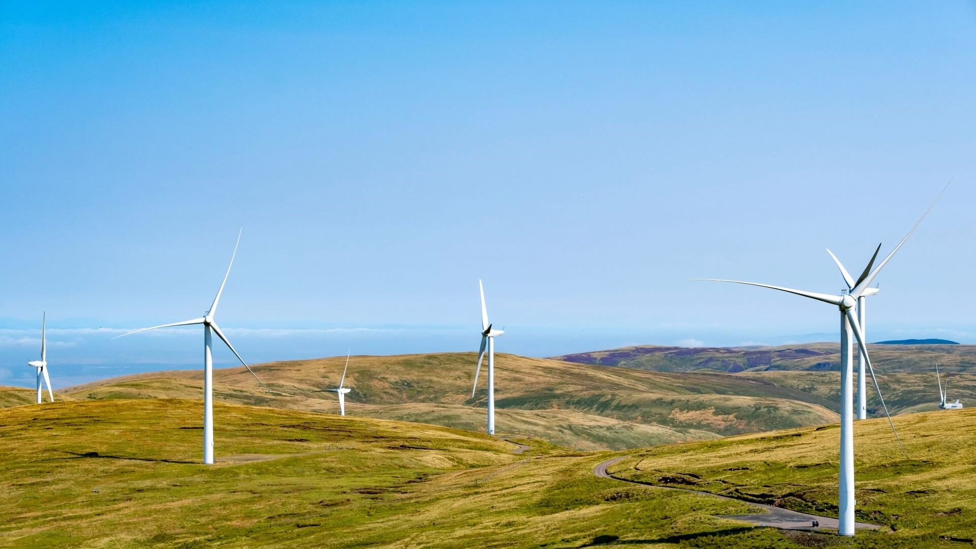 Series of wind turbines in Scottish hills, set against blue sky