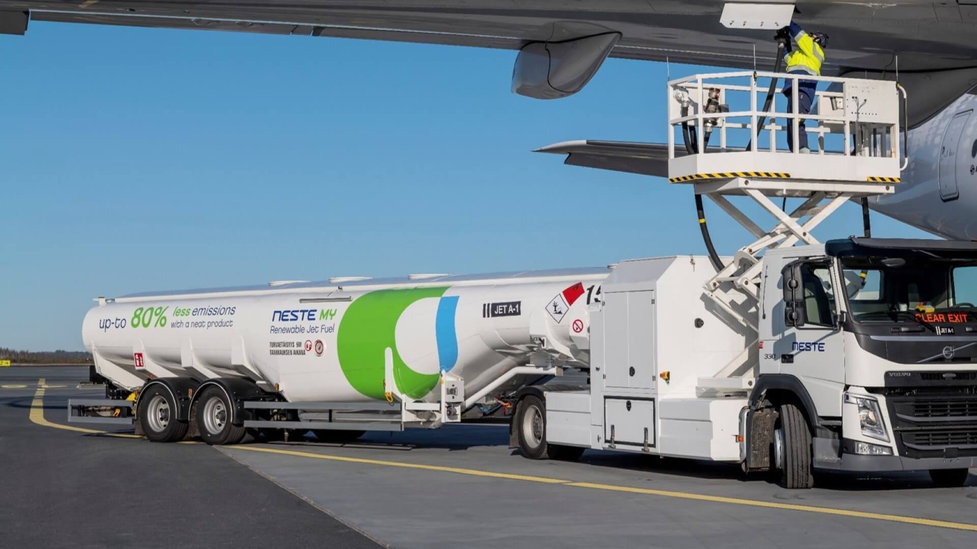 Close up of underside of aeroplane wing being refuelled with sustainable aviation fuel, with tanker alongside aircraft