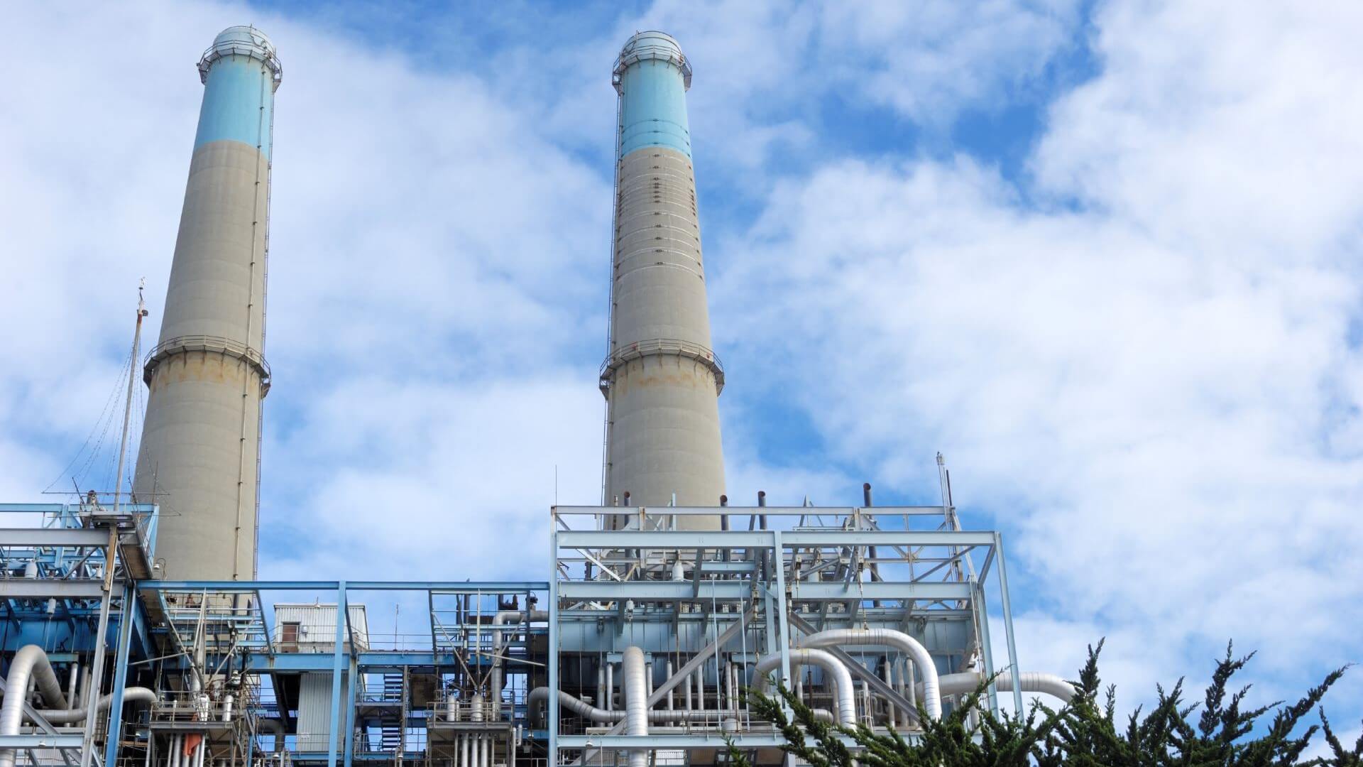 Two large industrial chimneys and building pipework set against blue sky and white clouds