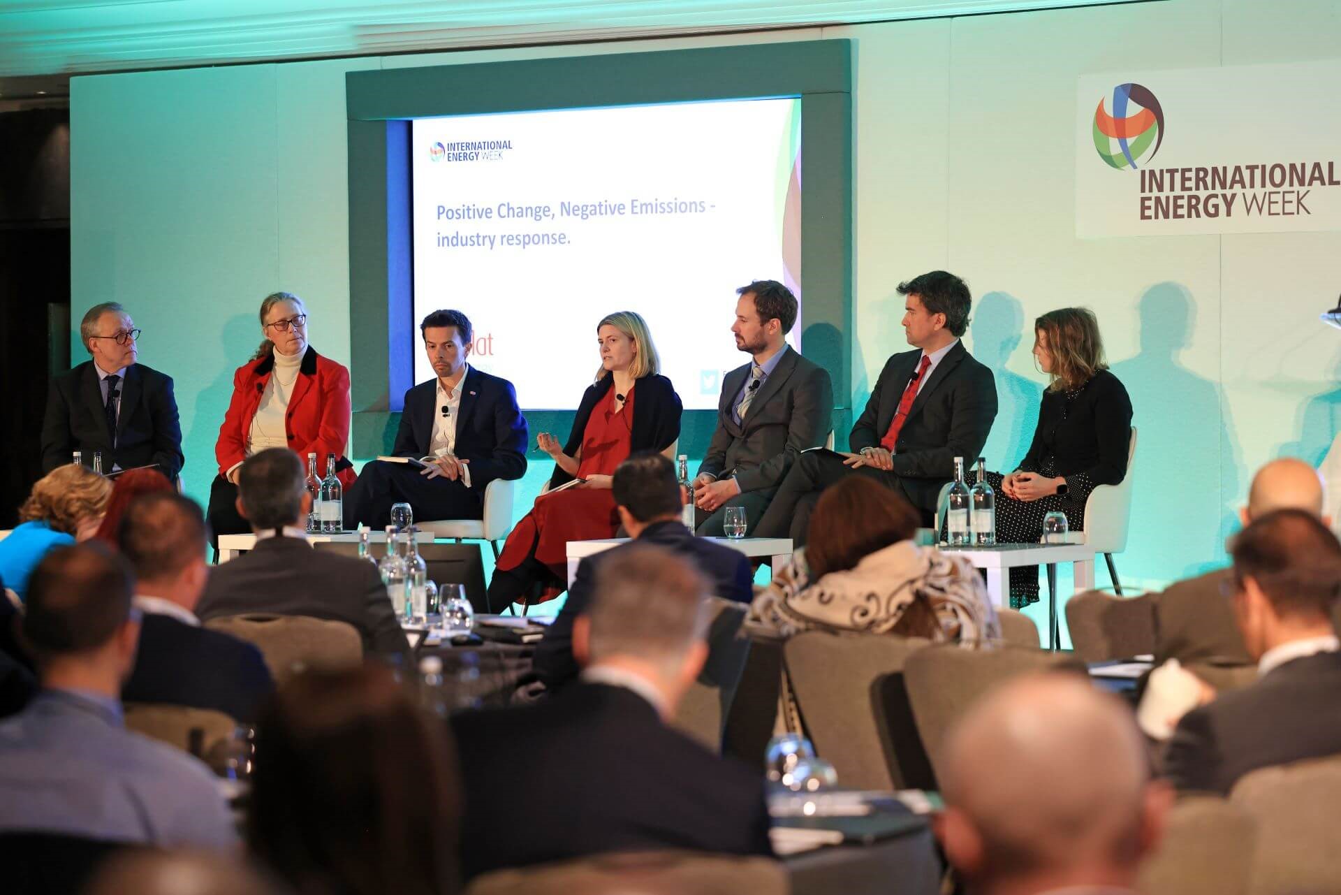Panel of speakers sitting on stage with presentation screen behind and audience in front