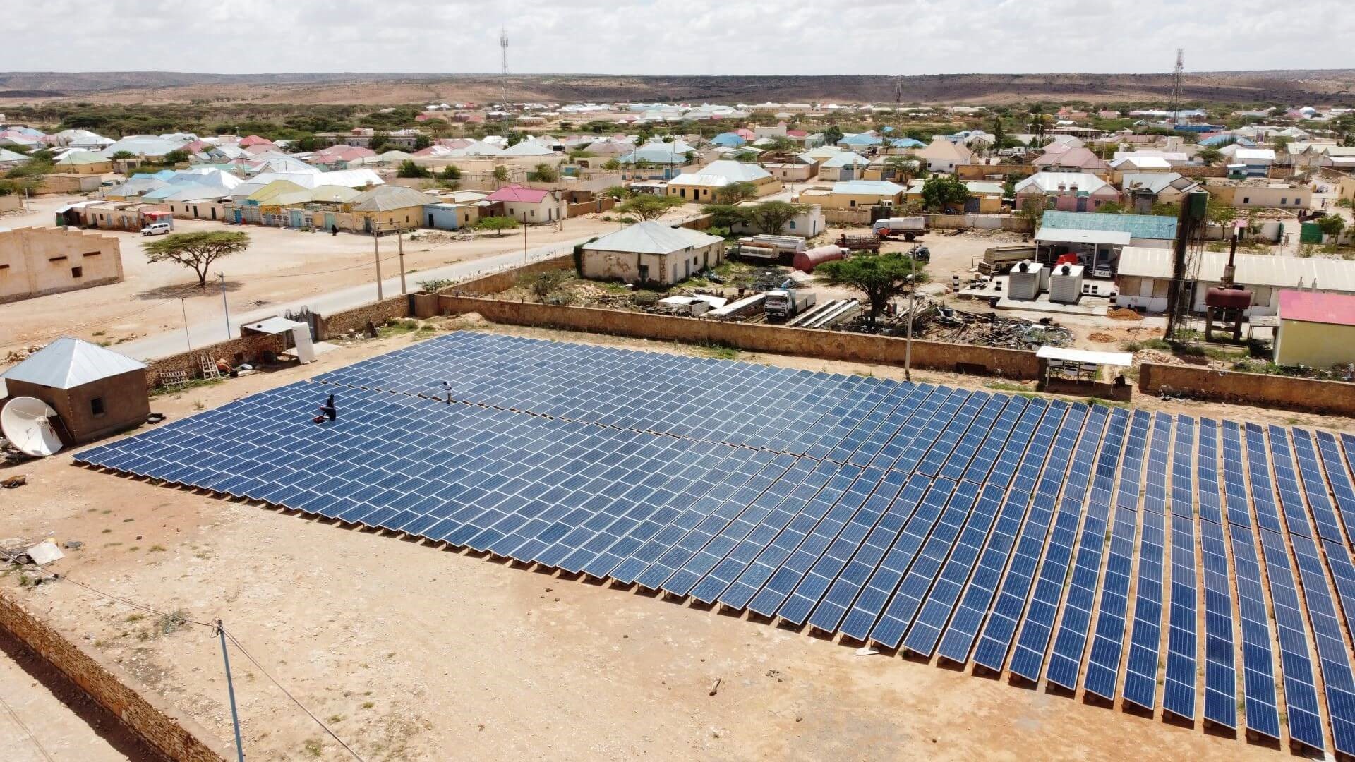 Rows of solar panels on solar farm in Africa, with residential buildings in background