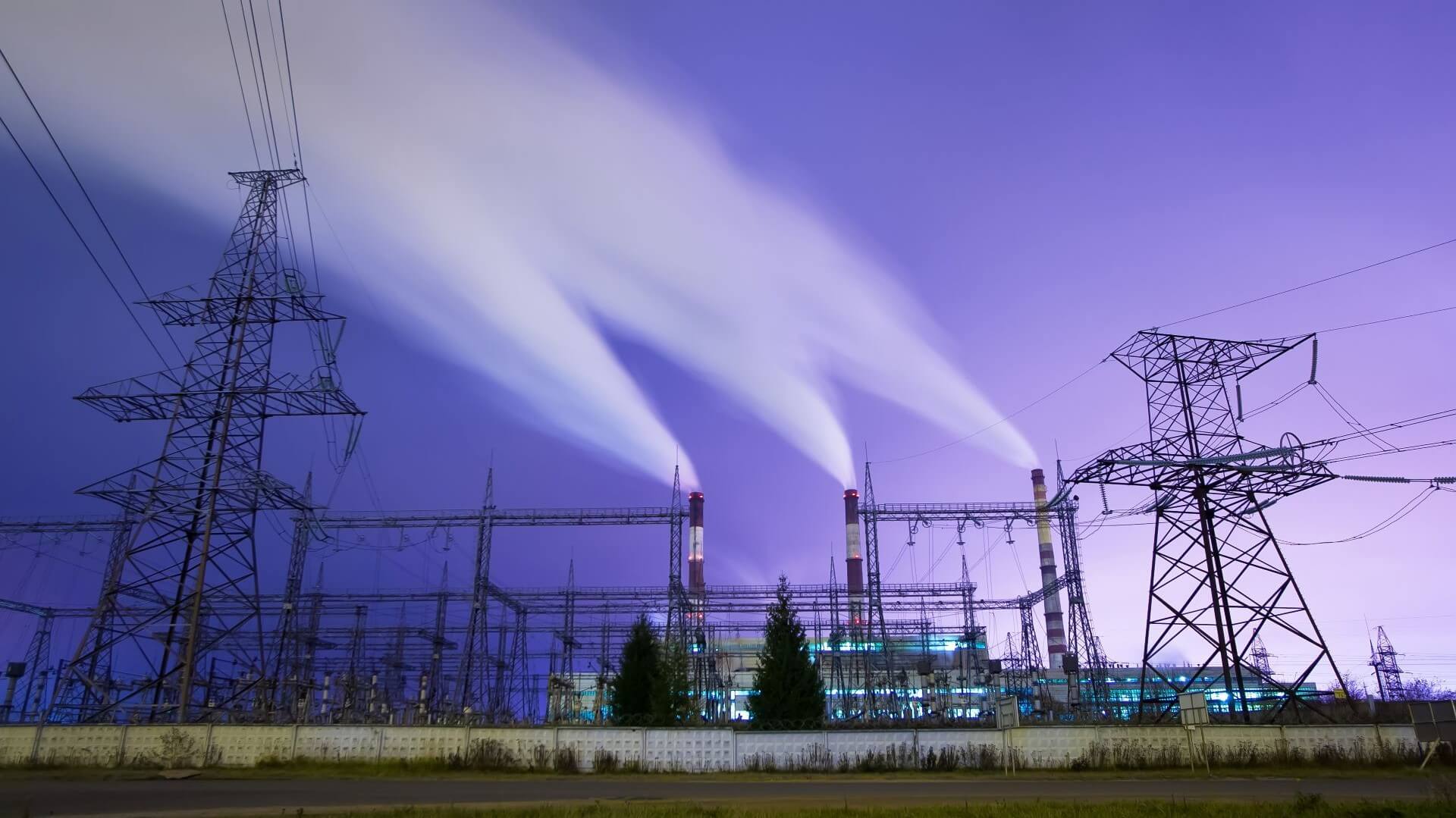 Electricity pylons and cables in front of chimneys emitting smoke