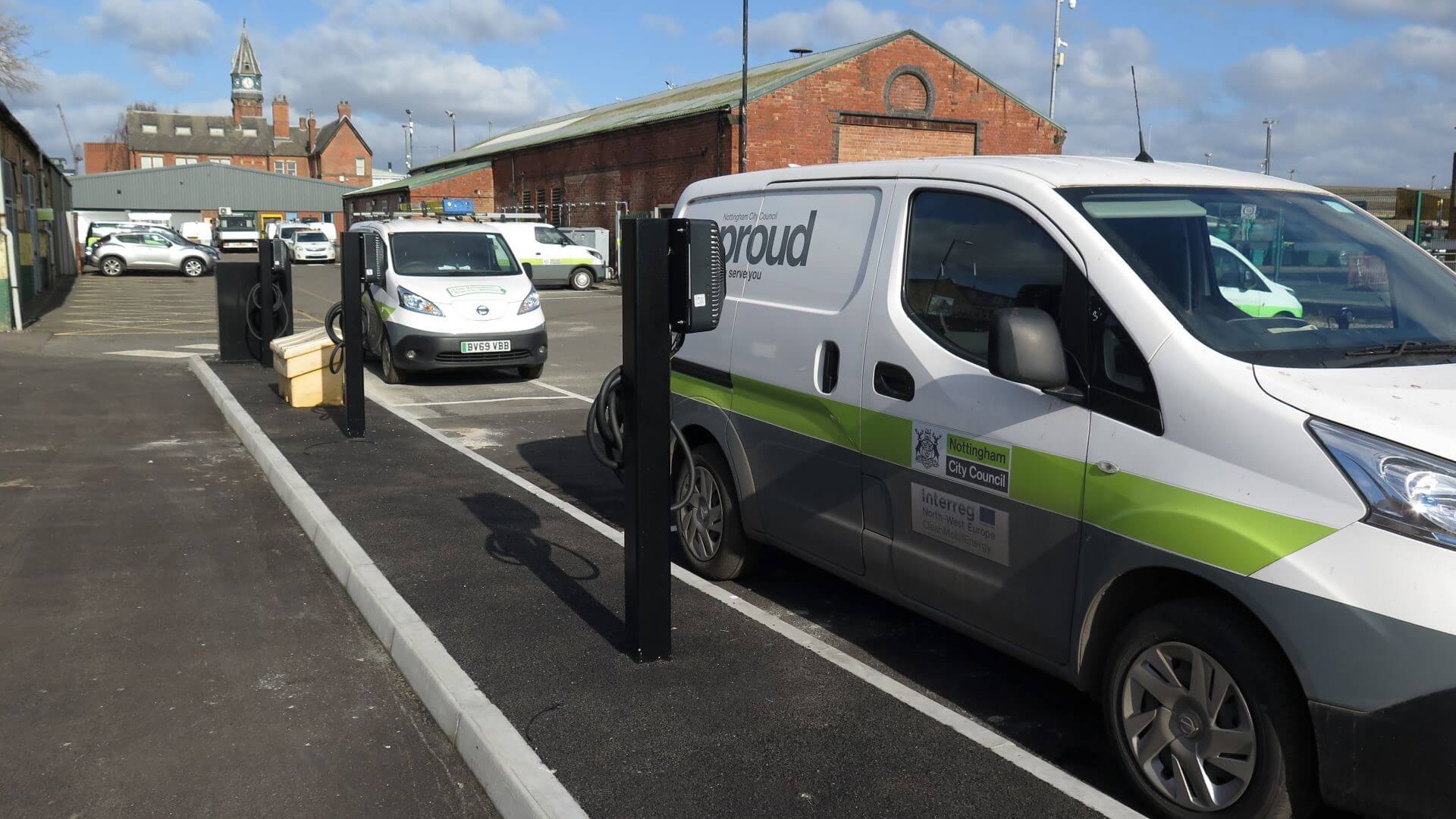 Two electric powered vans parked alongside pavement and charging from kerbside charging units