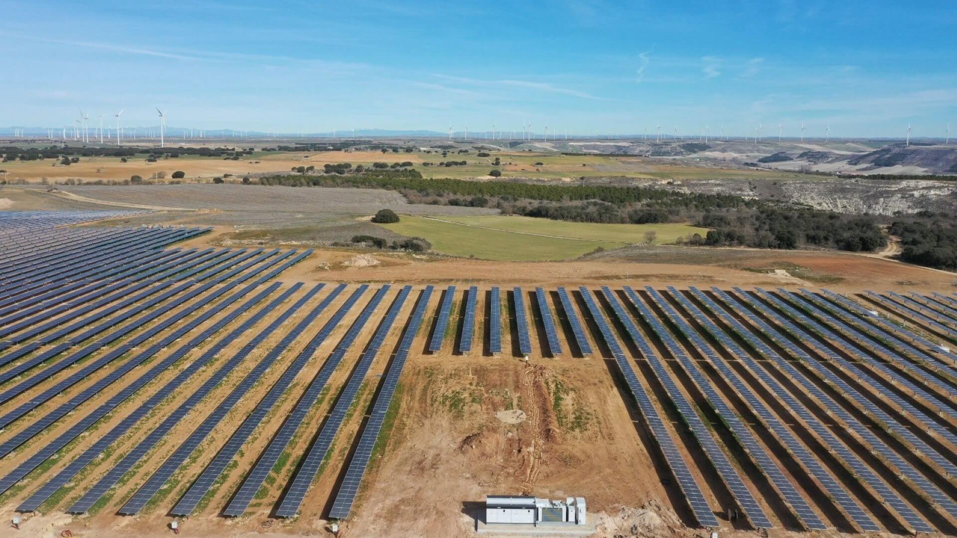 Aerial view of solar panels in field with nearby wind farm
