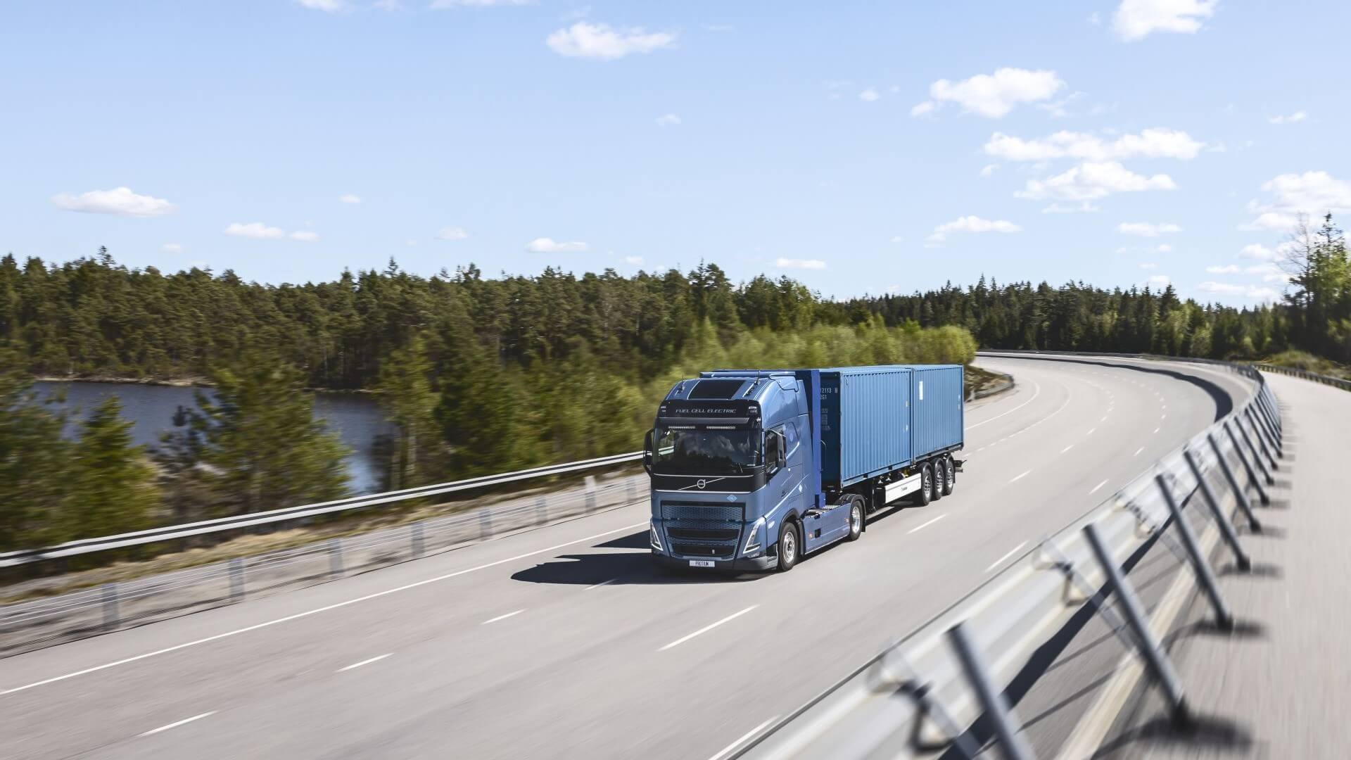 Heavy duty truck driving along empty dual carriageway with green trees in background