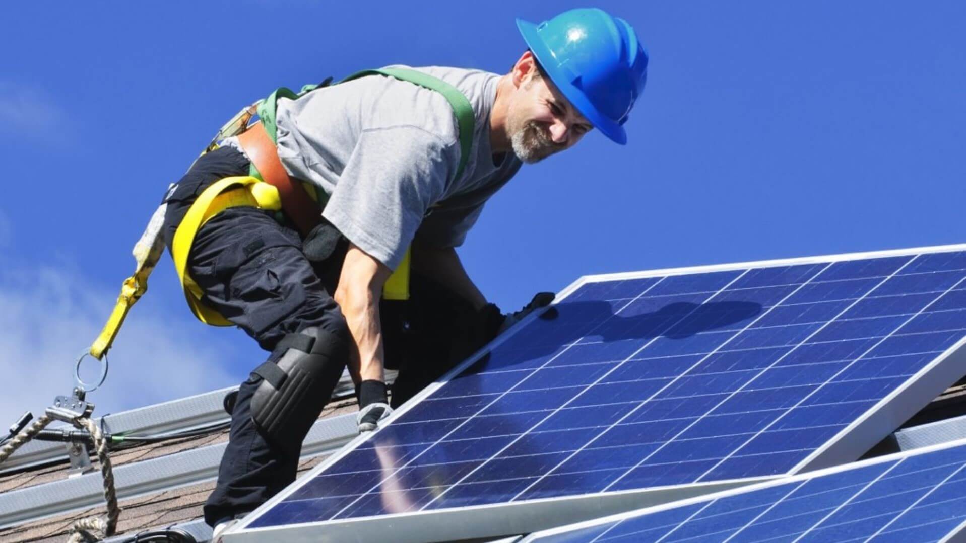 Man in hard hat and safety harness on roof installing a solar panel