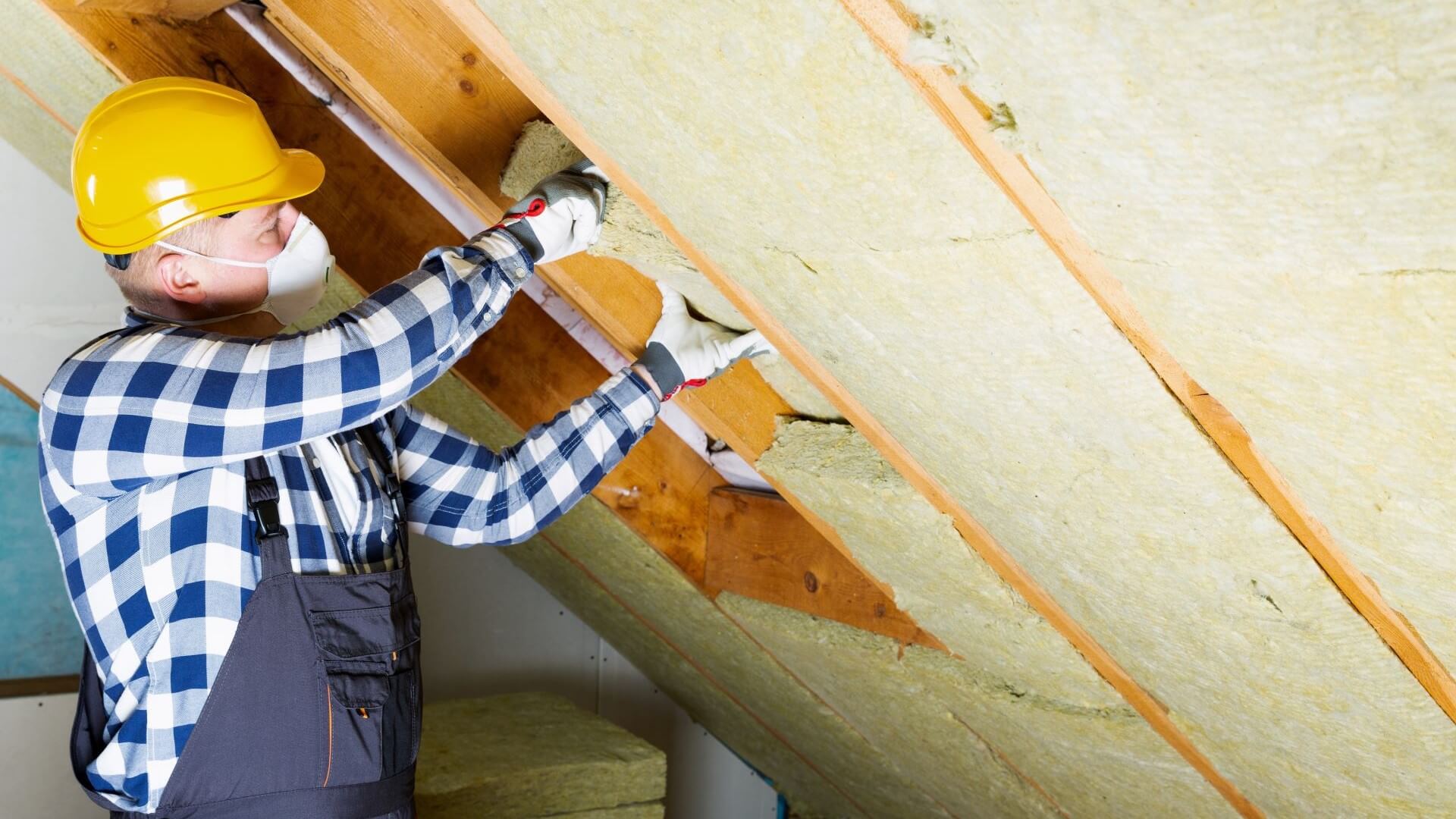 Man in hard hat installing roofing insulation in house