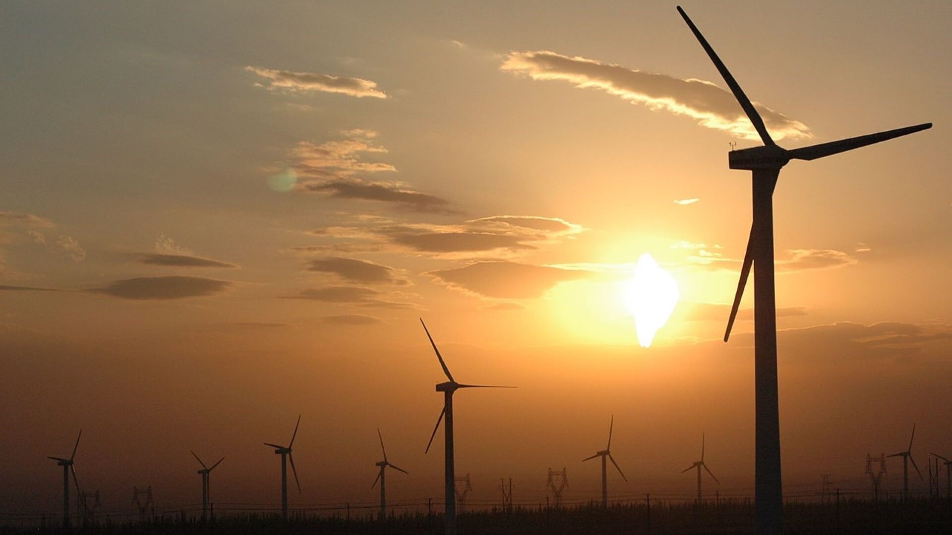Silhouettes of wind turbines set against orange sunset sky