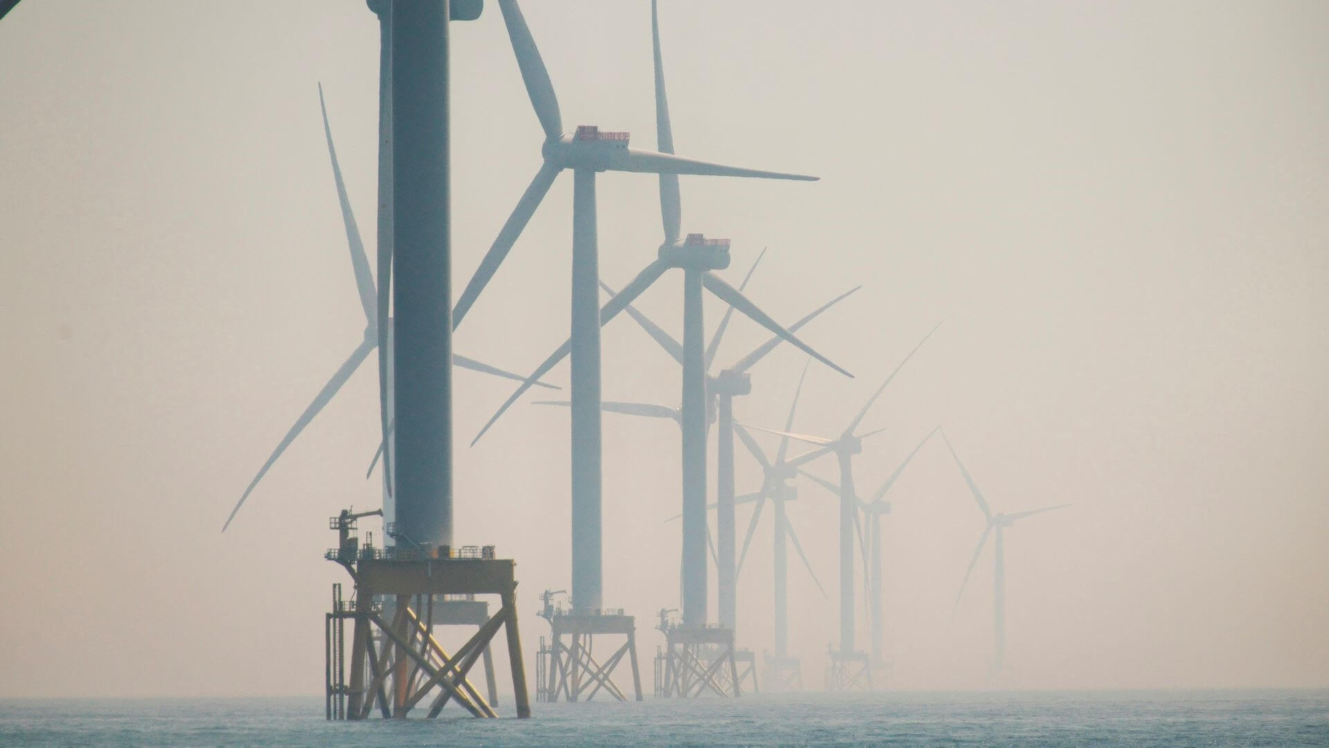 Offshore wind turbines on calm sea seen through grey misty haze