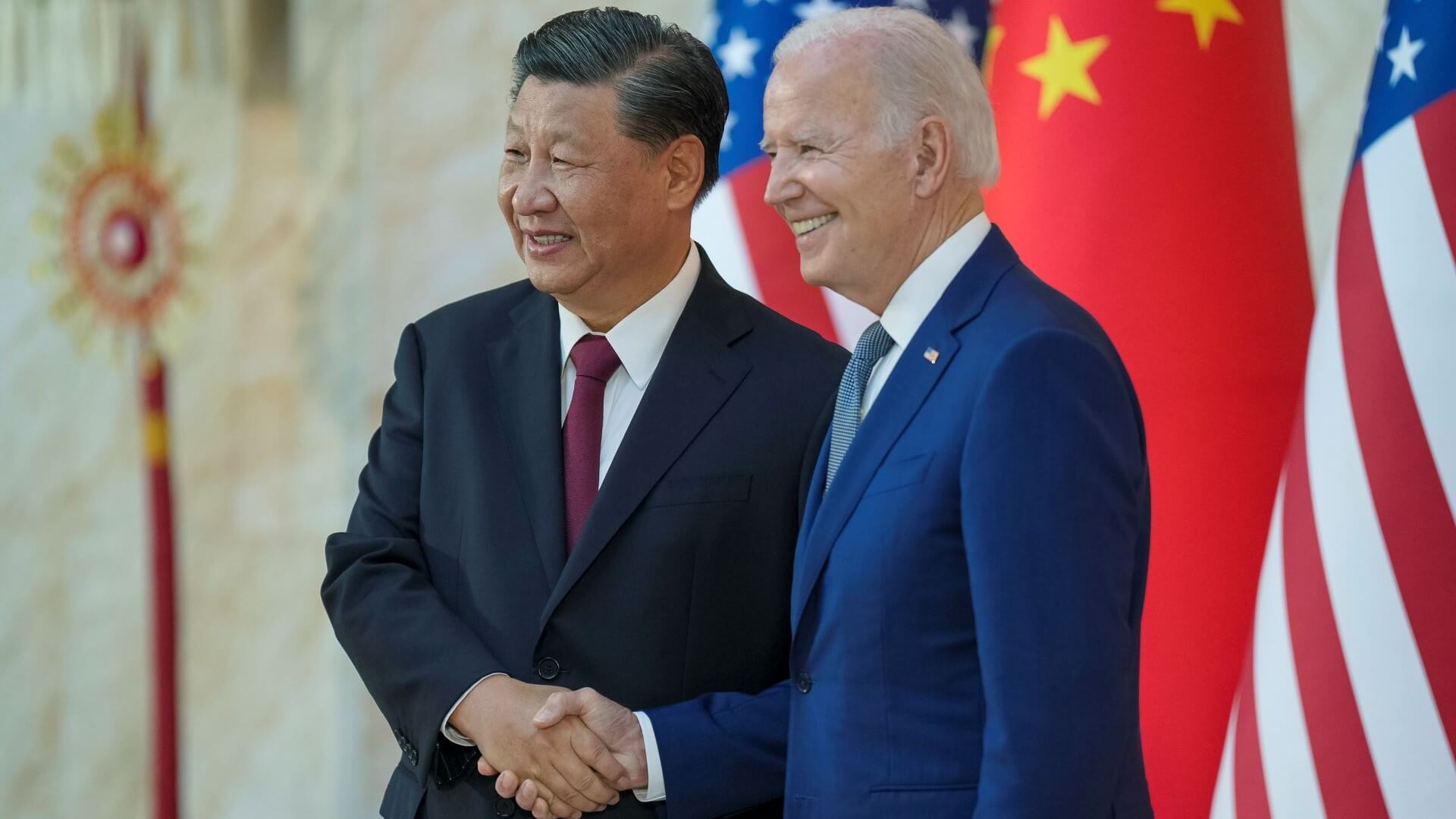 US and Chinese presidents shaking hands and smiling in front of national flags