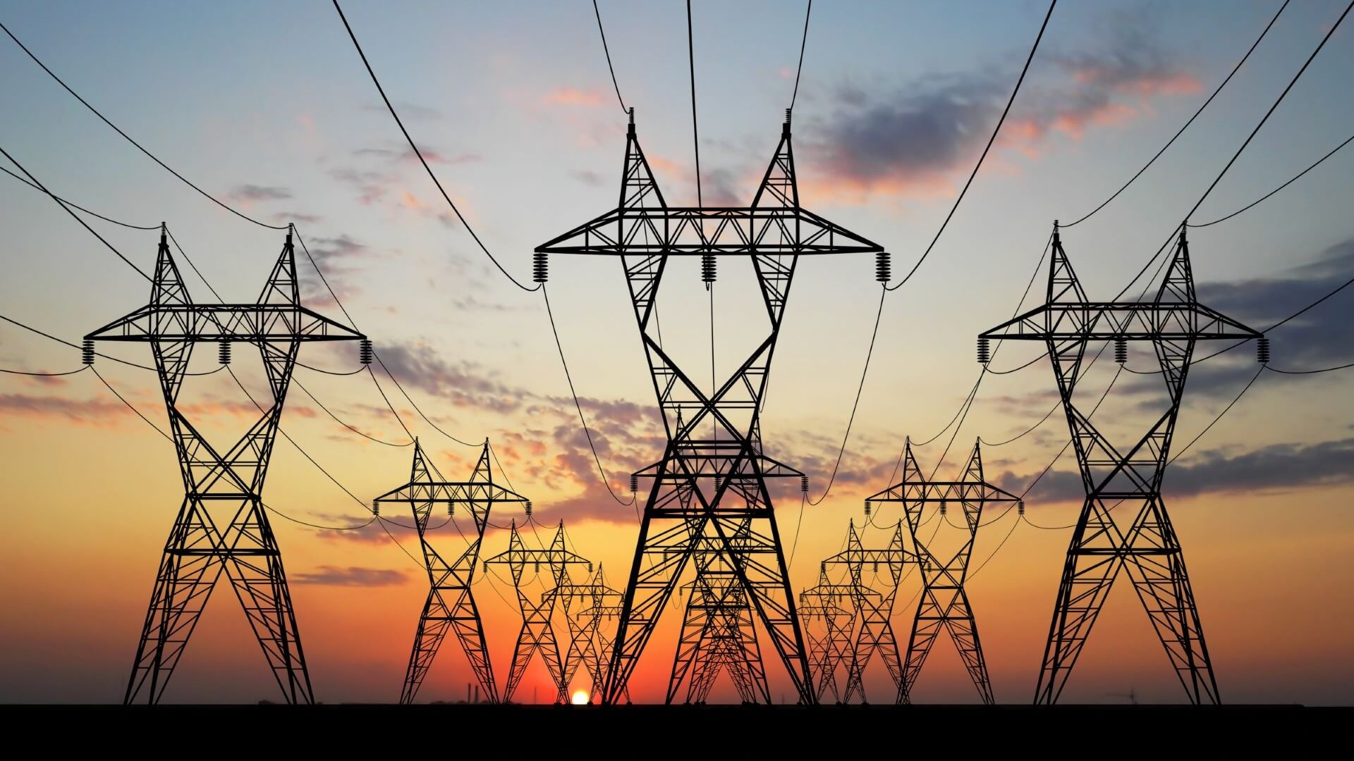 Silhouetted rows of electricity pylons and cables stretching into the distance against a sunset