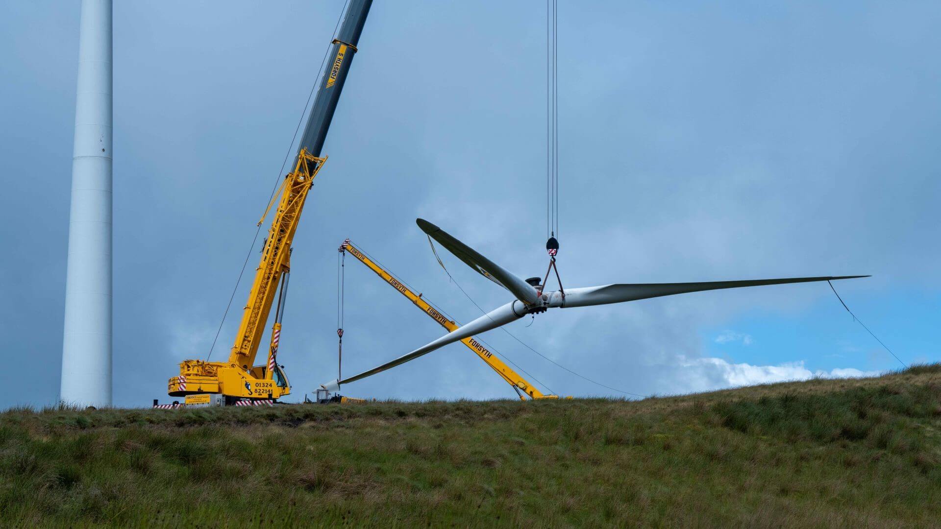 Crane lifting blades down from wind turbine and setting them on the ground