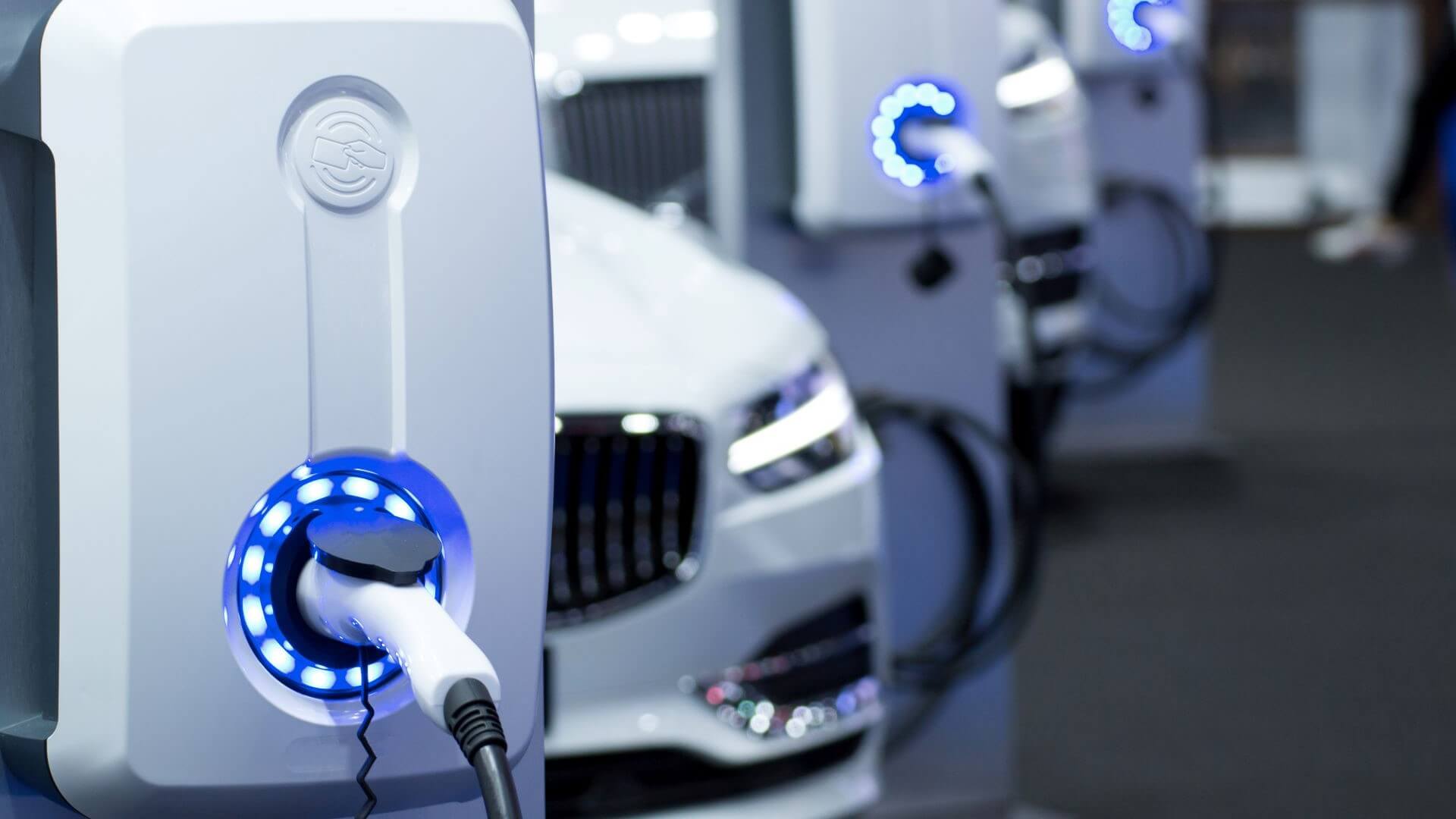 Close up of EV chargepoint with row of cars plugged in behind