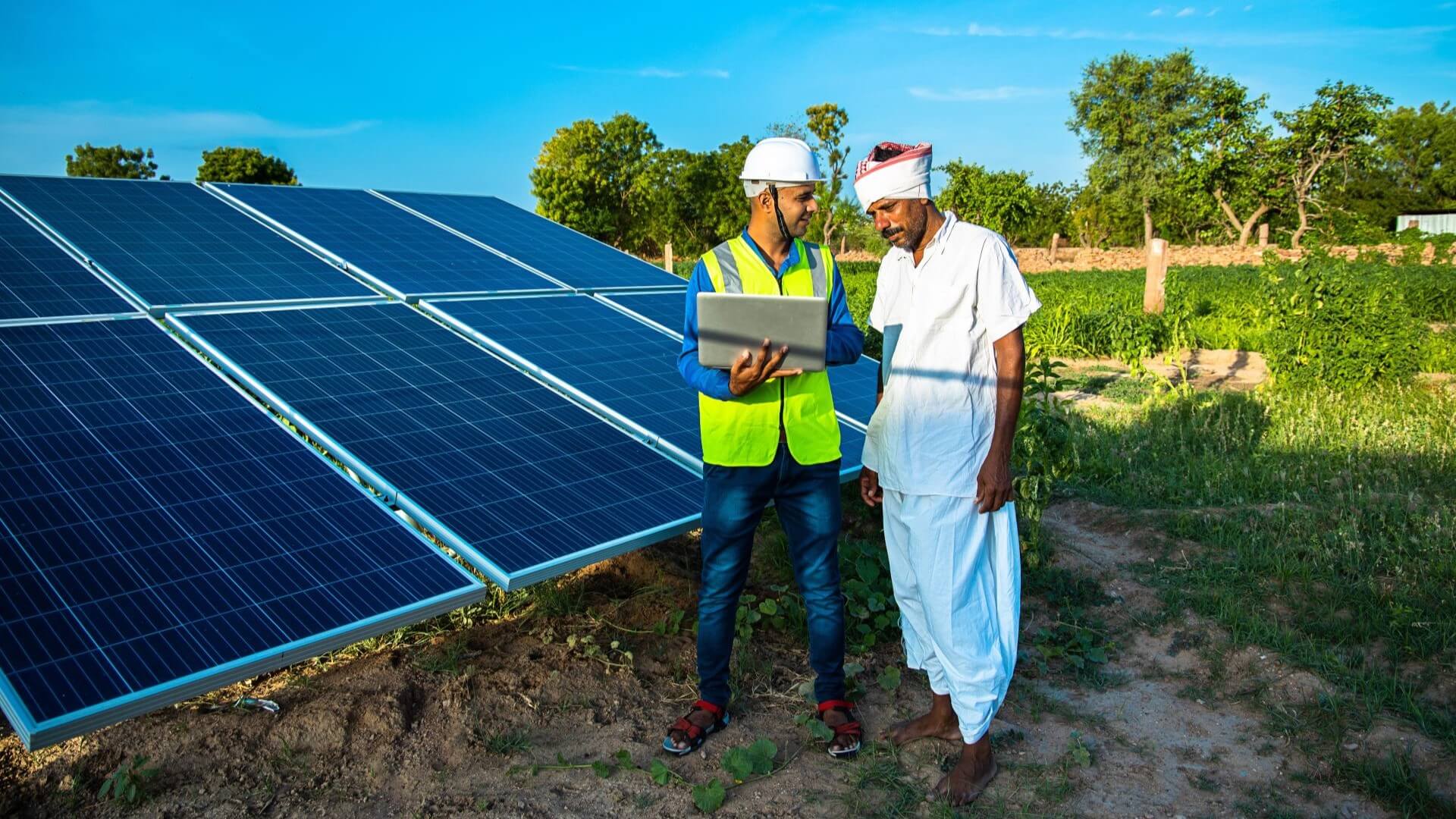 Two people in solar field in India discussing project whilst looking at laptop