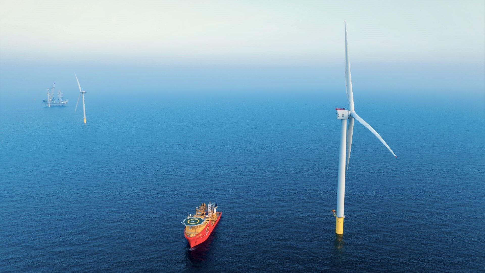 Large wind turbine in foreground with vessel nearby and other turbines in back ground