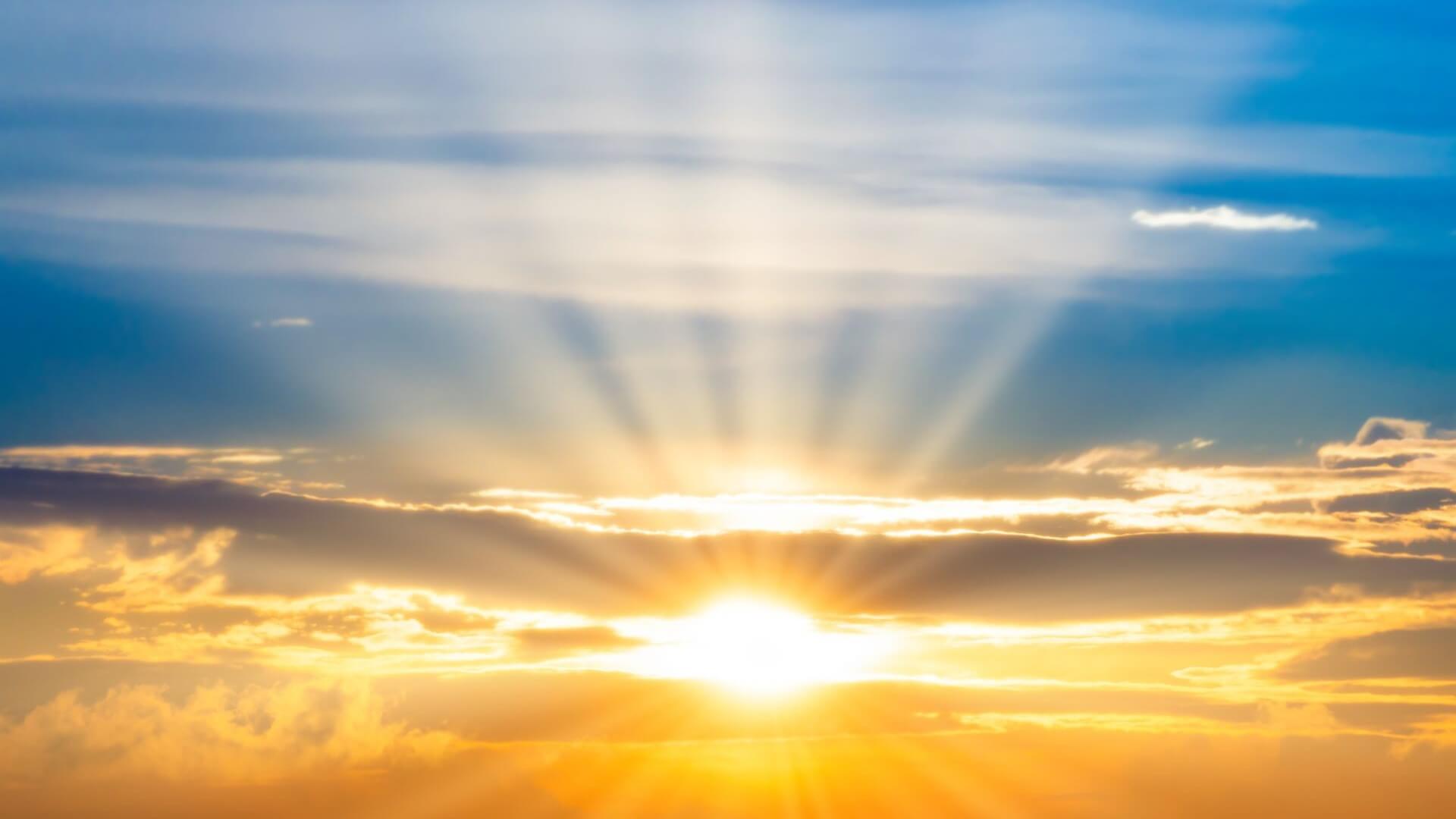 Bright sun with blue sky above and bright clouds and yellow sky below
