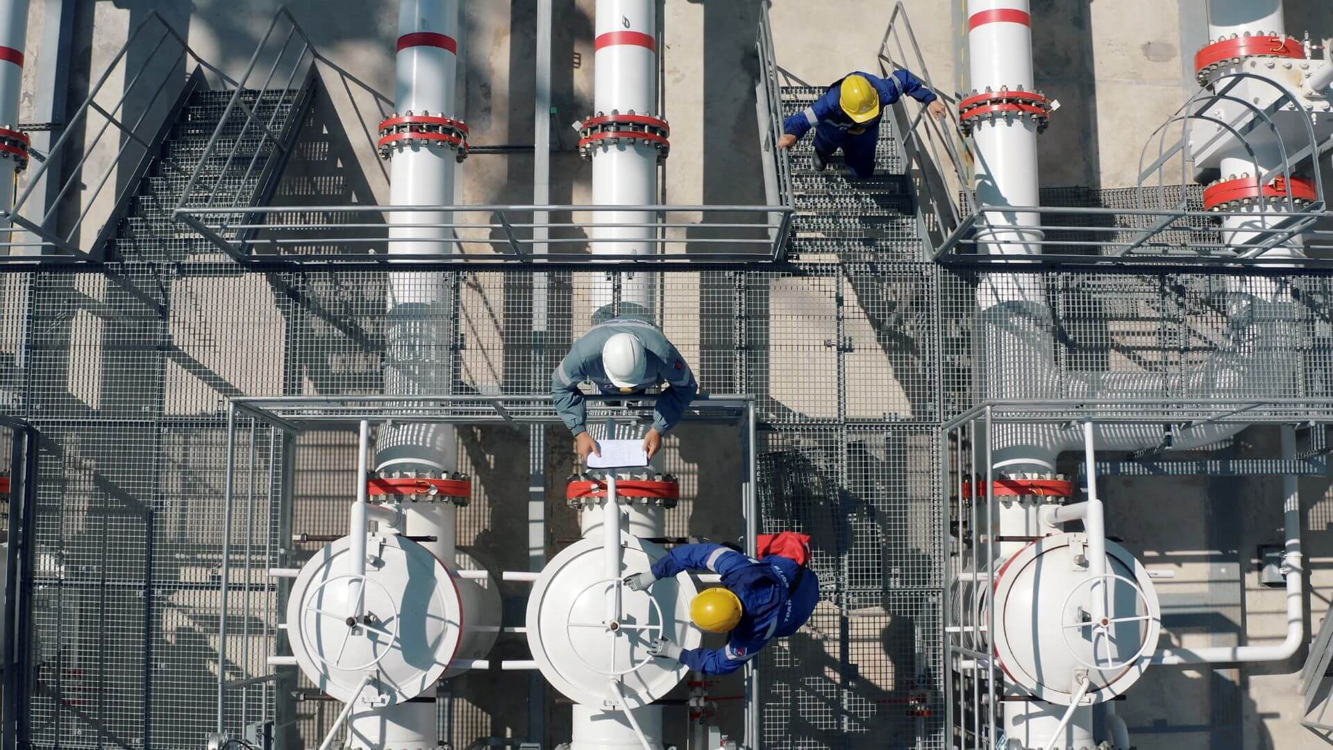 Overshead view of three people in hard hats by pipework and valves