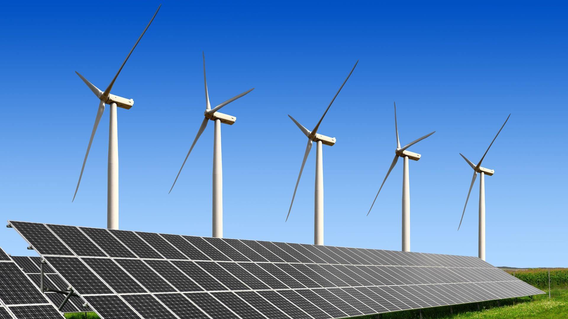 Row of solar panels and wind turbines against a blue sky