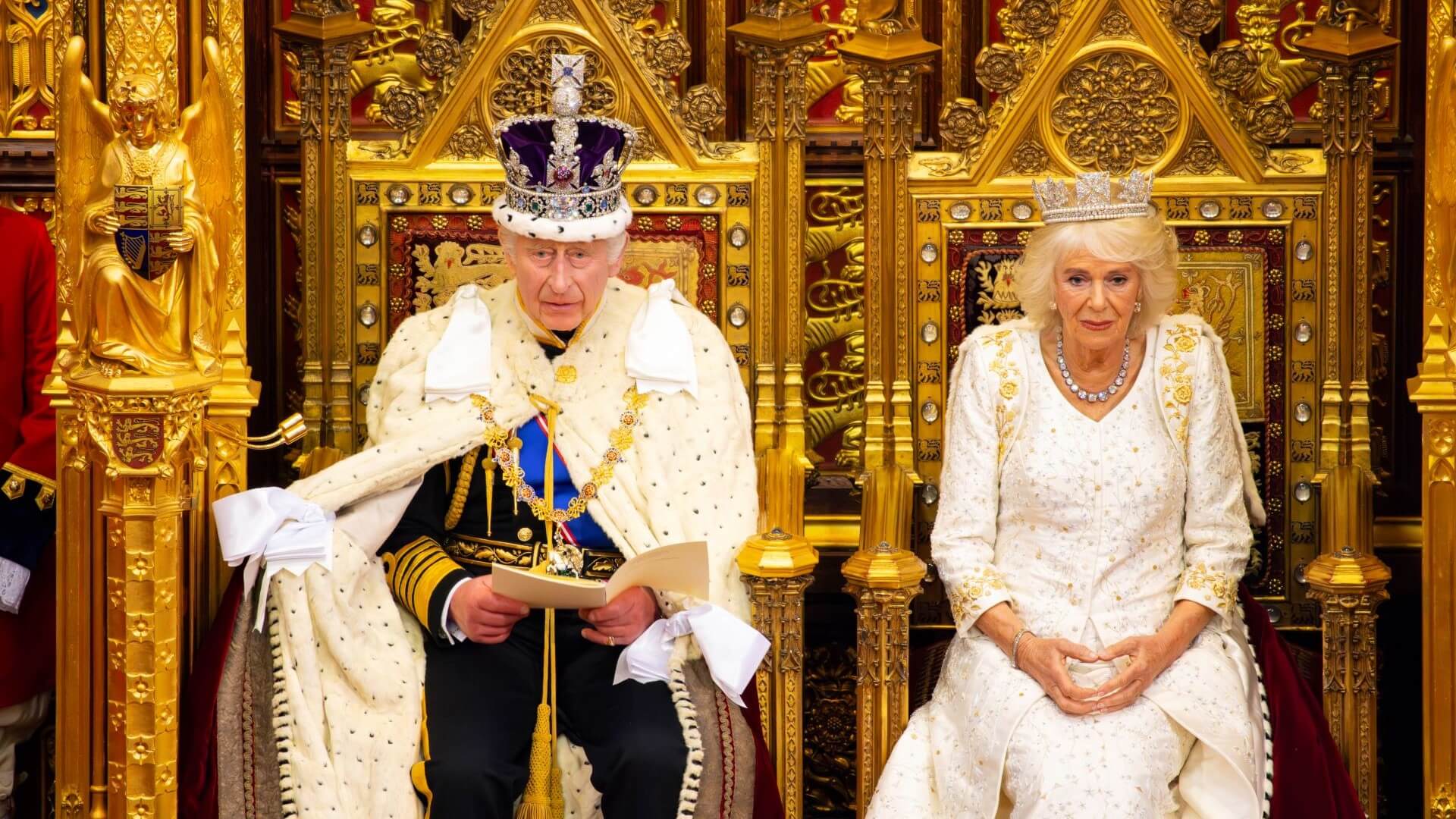 King Charles III and Queen Camilla in royal robes sitting on thrones in Houses of Parliament