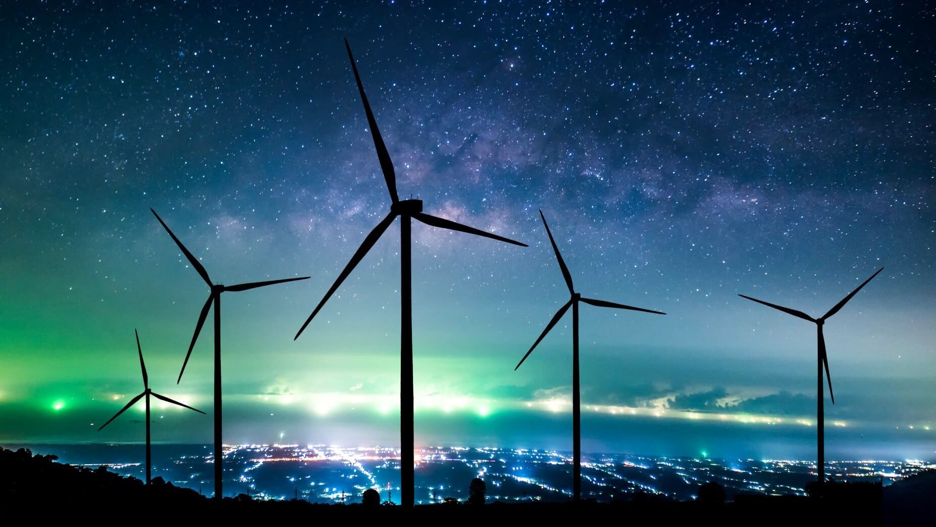 Onshore wind turbines at night against backdrop of lit up city