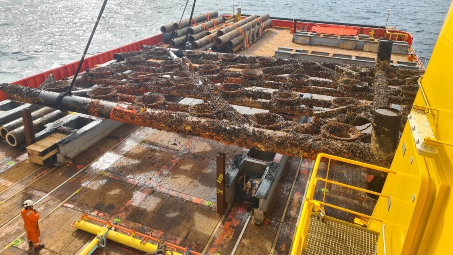Close up of flat grid section of offshore structure frame, covered in marine growth, on deck of decommissioning vessel