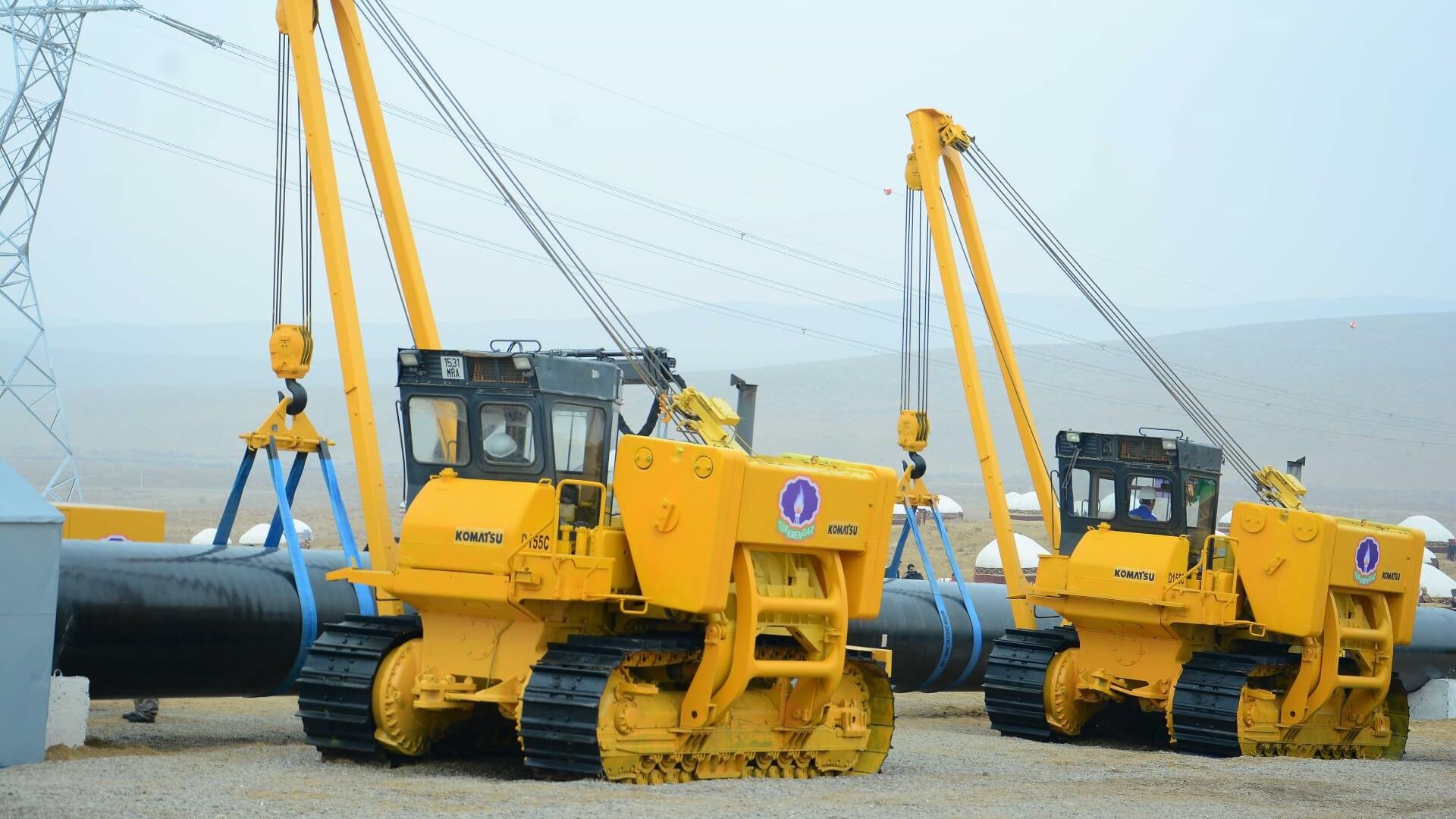 Two cranes on tracks lifting large pipework