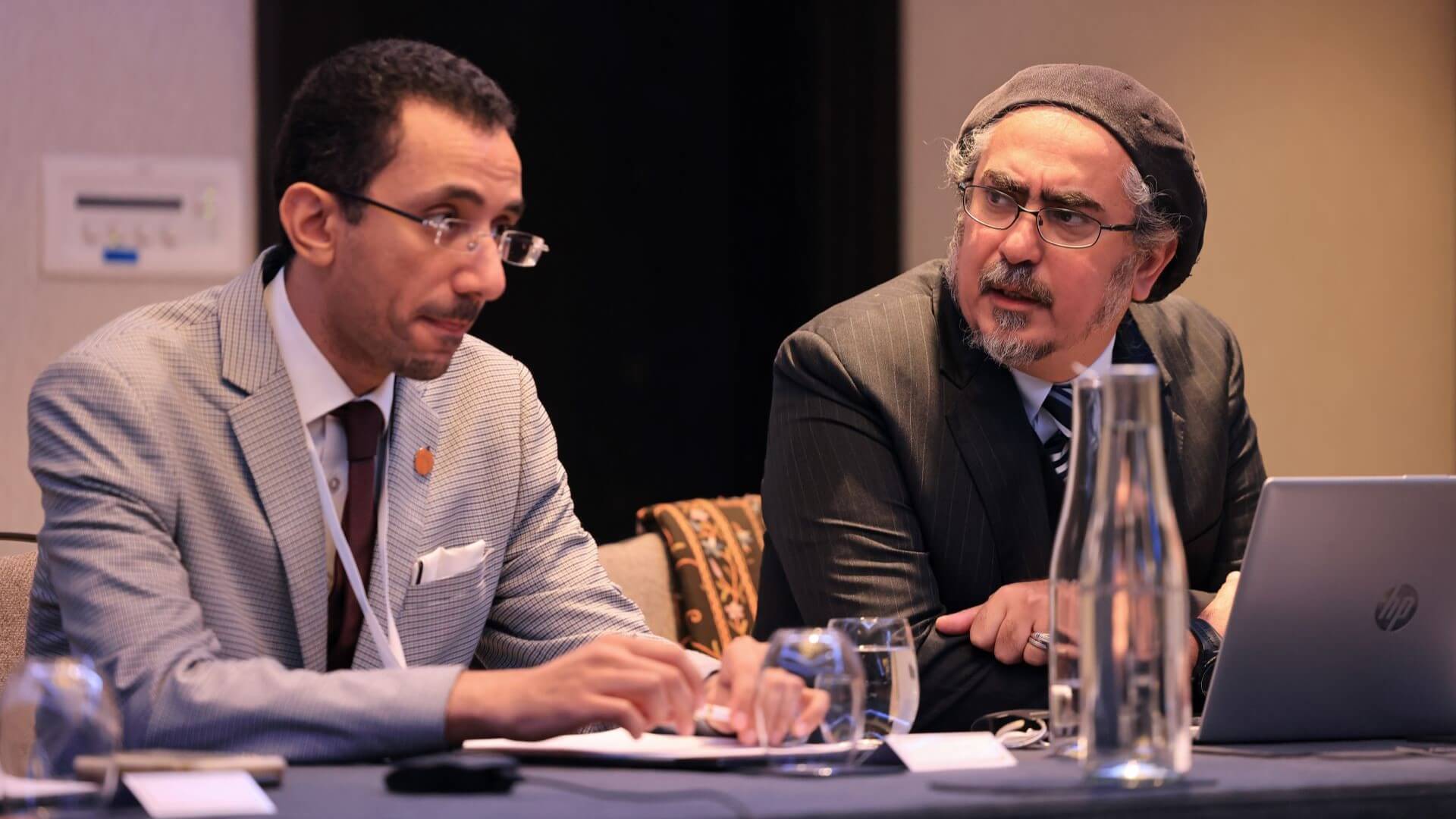 Dr Yousef M Alshammari sitting behind desk on stage on left, watched by Dr Waddah S Ghanem Al Hashmi on right